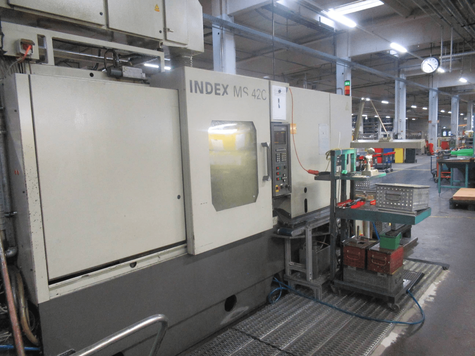 INDEX MS 42C CNC-Maschine in einer Werkstatt, Seitenansicht mit Bedienfeld und Werkzeugablage auf Rollwagen.