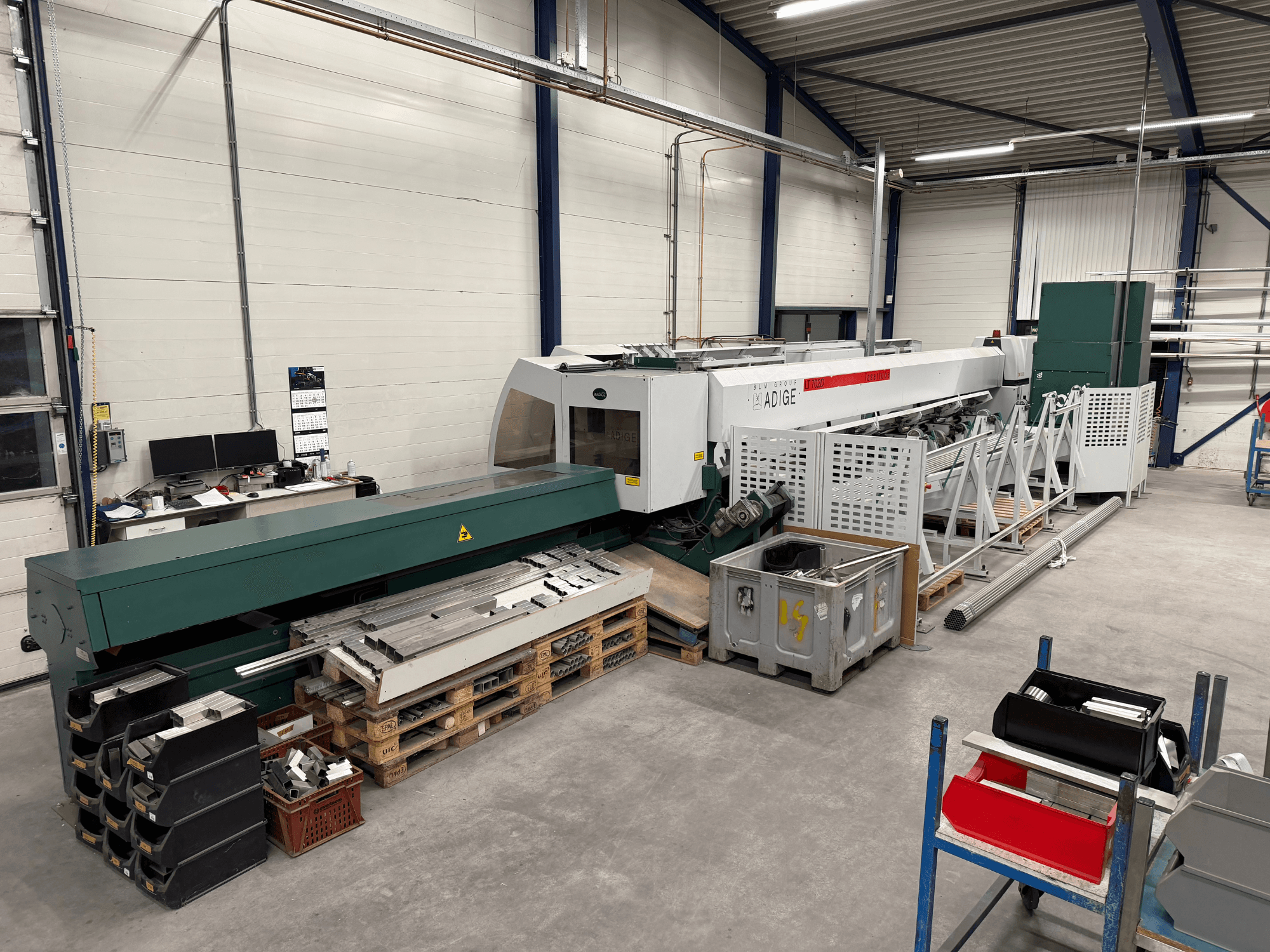 BLM Adige LT702 CO₂-Laserschneidmaschine in einer Werkstatt, Seitenansicht mit sichtbaren Metallteilen und Unordnung im Arbeitsbereich.