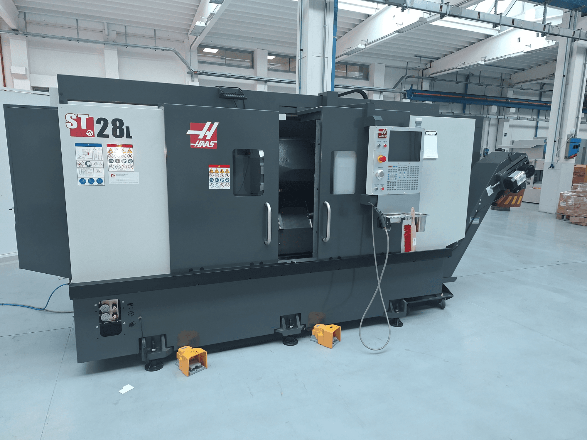 Seitenansicht der horizontalen Drehmaschine Haas ST-28L mit Bedienfeld, Bedientasten und Sicherheitshinweisen.
