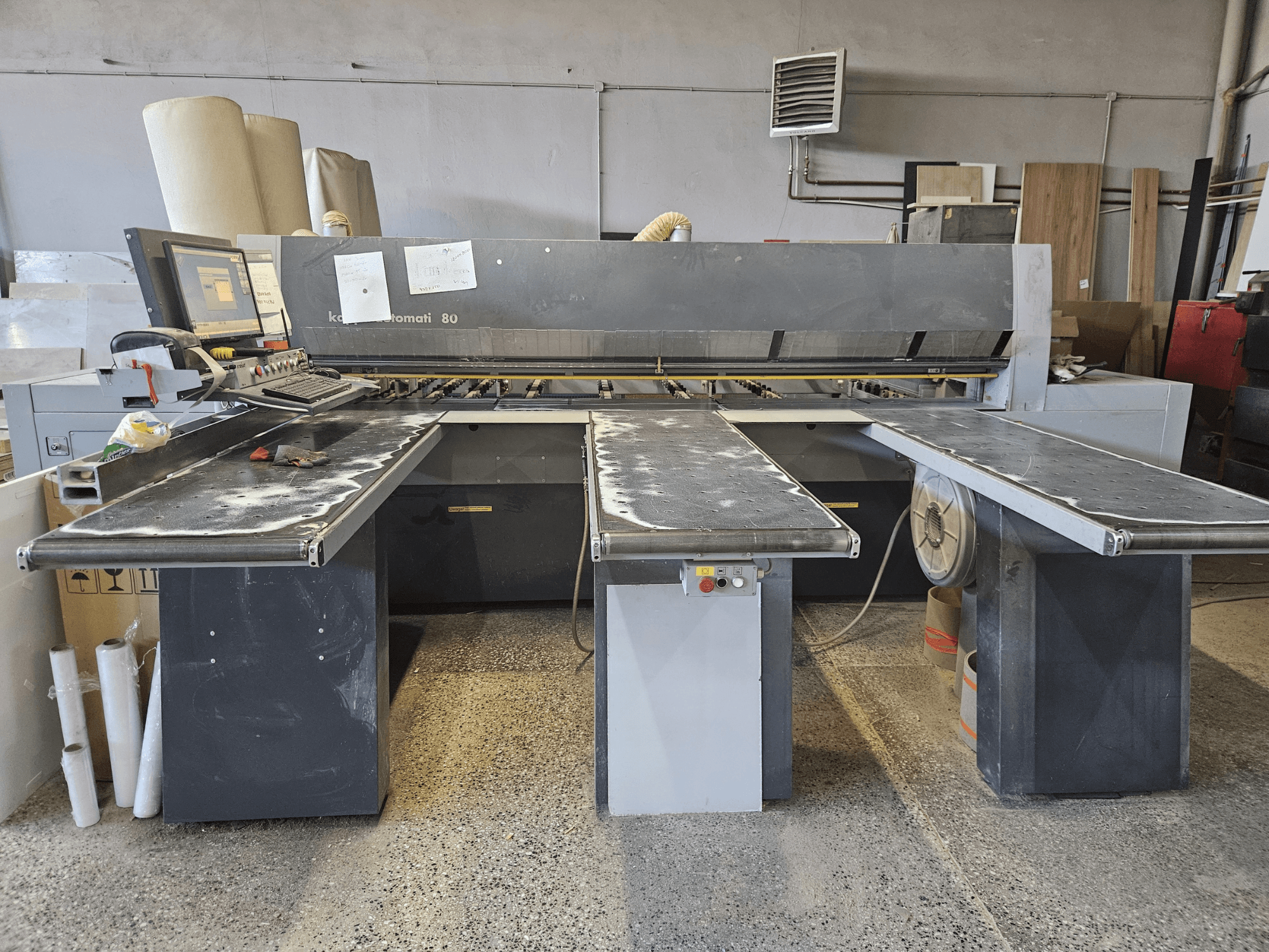 KAPPA Automati 80, Vorderansicht, mit drei flachen Tischen, Bedienfeld und verstreuten Sägespänen auf den Oberflächen.