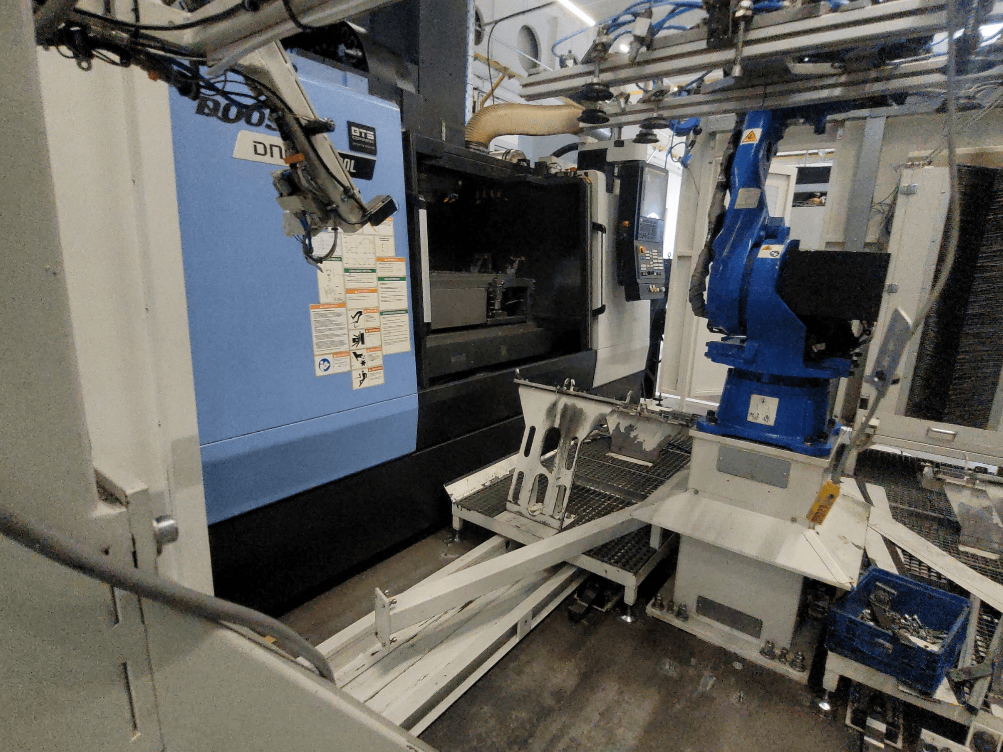 Seitenansicht des vertikalen Bearbeitungszentrums DOOSAN DNM 6700L, auf der der Roboterarm und das Bedienfeld zu sehen sind und die den Aufbau der Maschine veranschaulicht.