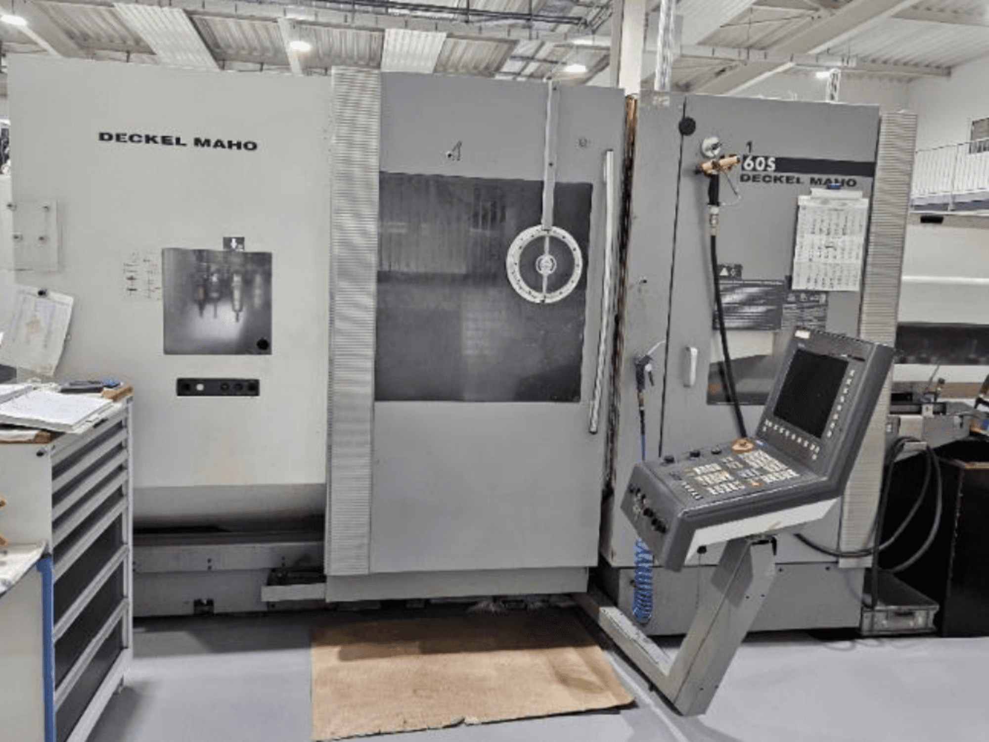 Vorderansicht einer DECKEL MAHO 60S CNC-Maschine mit Bedienfeld, Werkzeuge sichtbar, in einer Werkstatt.