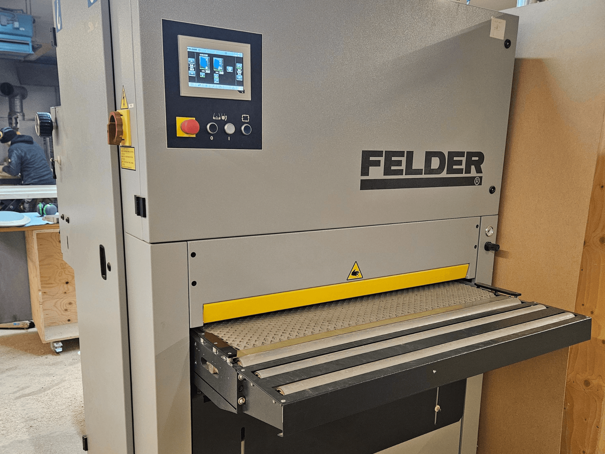 FELDER Holzbearbeitungsmaschine in der Frontansicht, mit digitalem Bedienfeld und gelbem Vorschubtisch mit Sicherheitshinweisen.