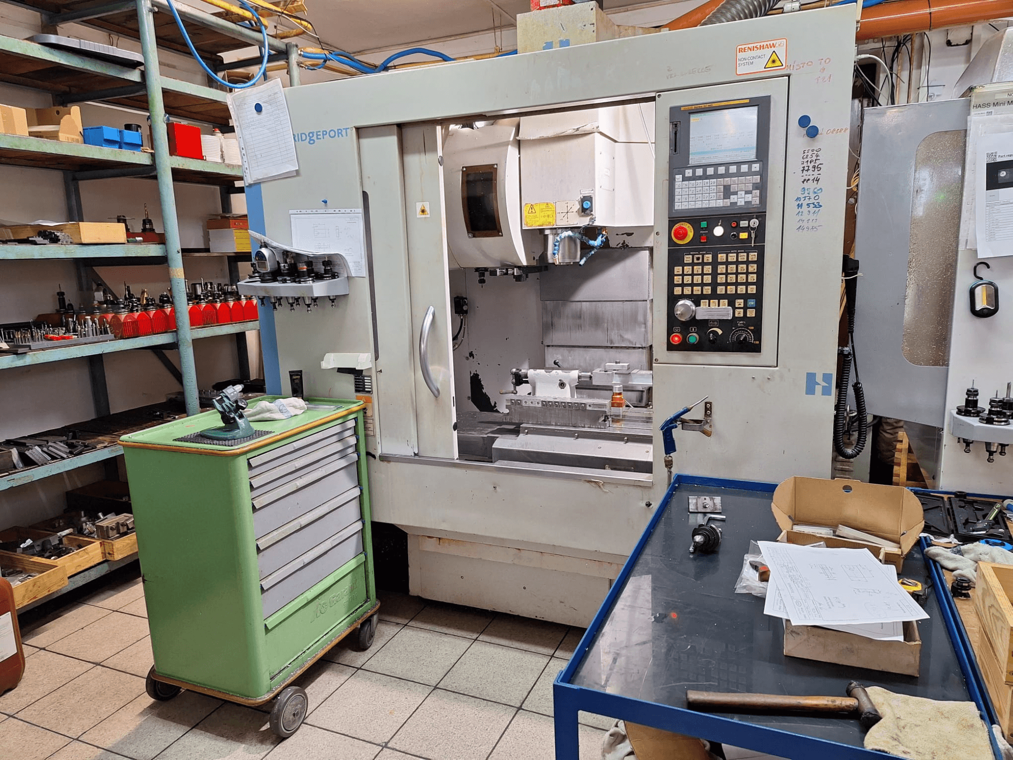 Vorderansicht des vertikalen Bearbeitungszentrums Hardinge Bridgeport GX 710 mit Bedienfeld, Werkzeugen und Regalen in einer Werkstattumgebung.