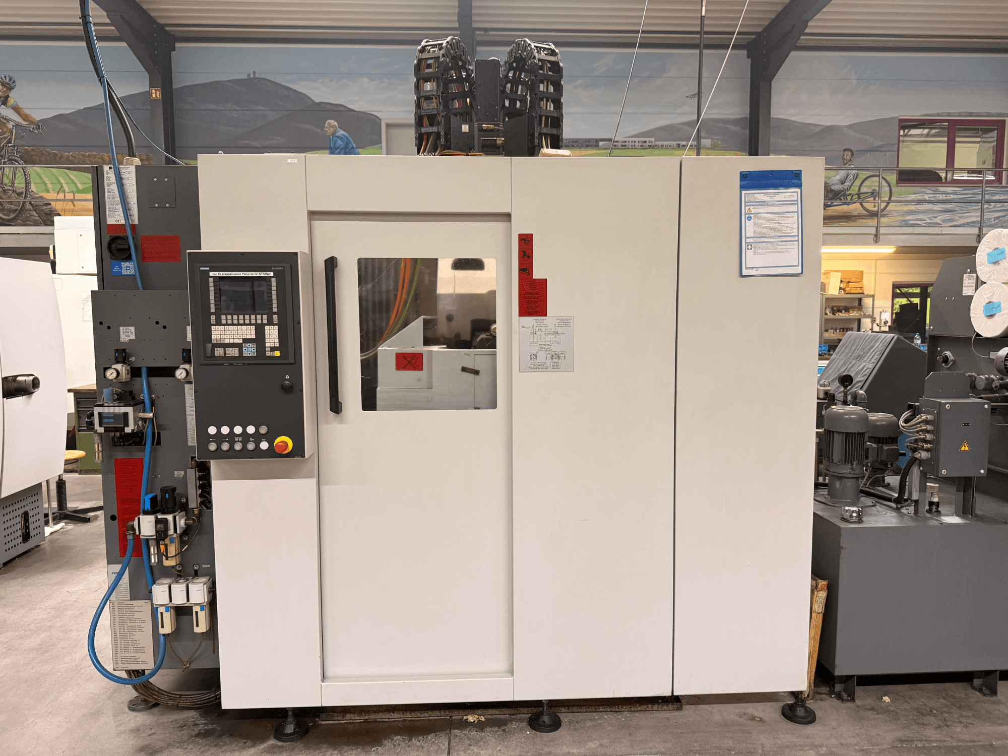 Weißes CNC-Bearbeitungszentrum mit Bedienfeld, Vorderansicht, mit Tasten und Digitalanzeige, in einer Werkstattumgebung.