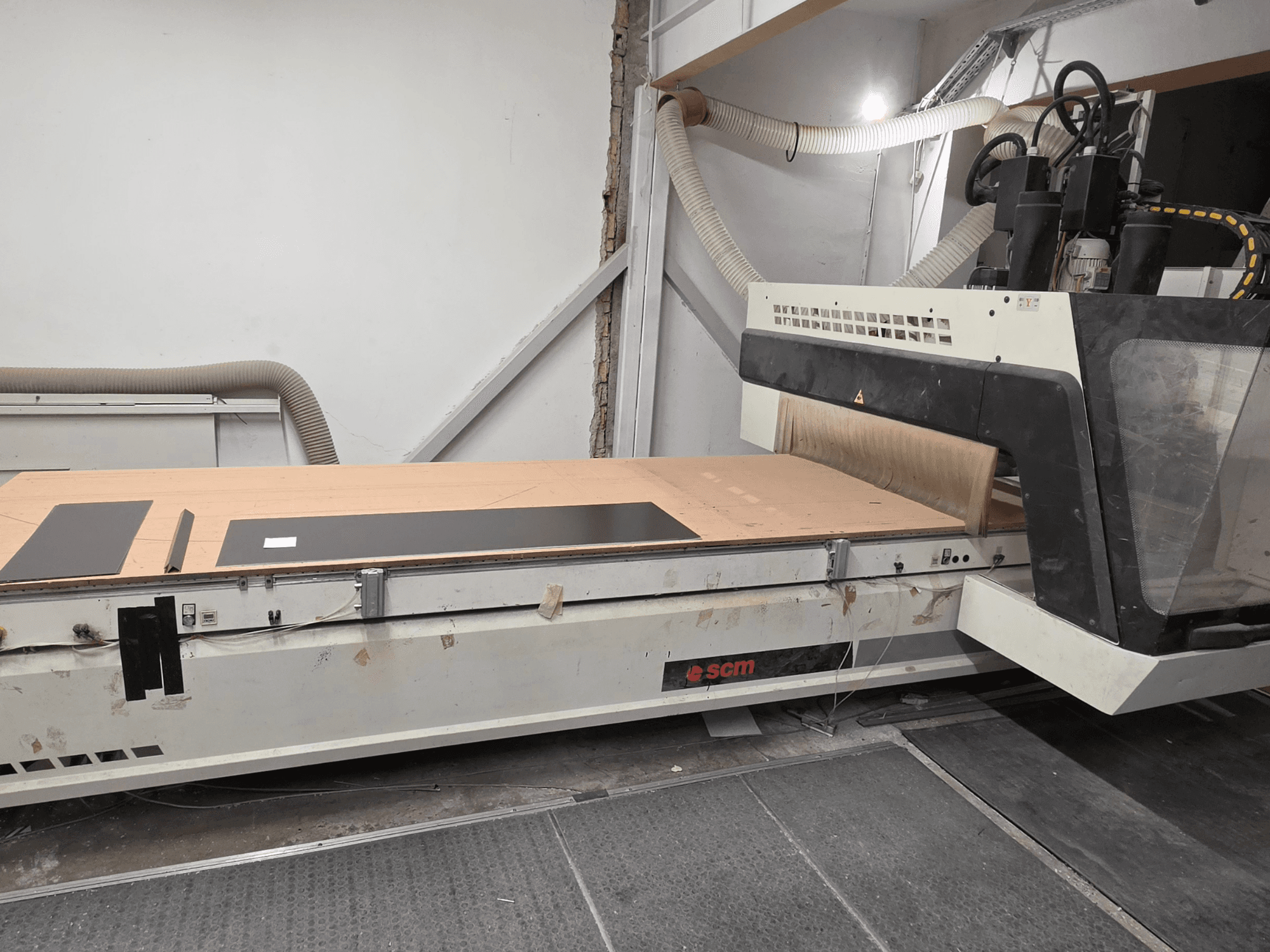SCM RECORD 132 CNC-Holzbearbeitungszentrum in Seitenansicht, mit flachem Arbeitstisch, schwarzen Werkstücken und Staubabsaugung.