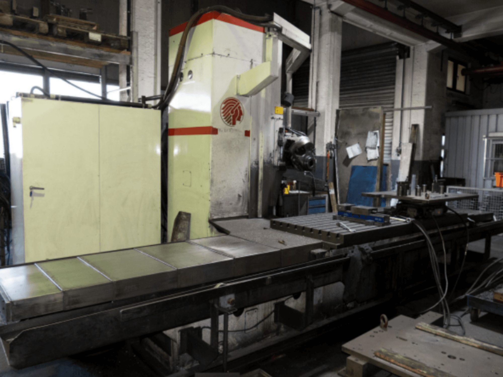 Industrielle Fräsmaschine mit großem Tisch, Seitenansicht, mit Bedienelementen und Anbaugeräten in einer Werkstattumgebung.