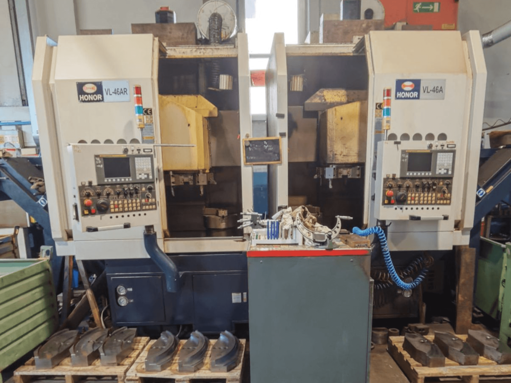 Vorderansicht der Vertikaldrehmaschine HONOR SEIKI VL 46A mit dem Bedienfeld und den umliegenden Bauteilen auf Holzpaletten.