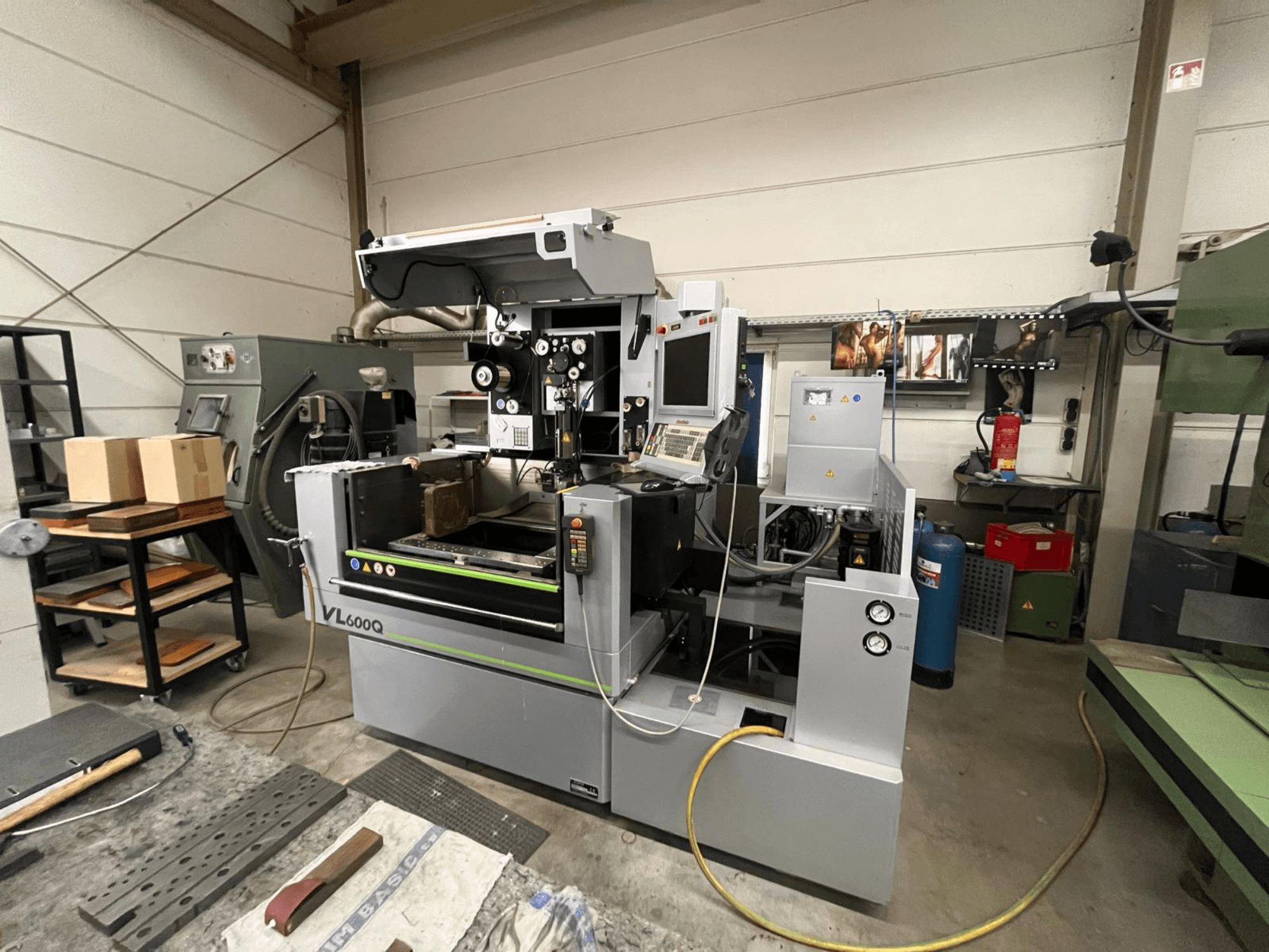 VL600Q CNC-Maschine in einer Werkstatt, Vorderansicht, mit Bedienfeld, eingelegtem Material und verschiedenen Werkzeugen in der Nähe.