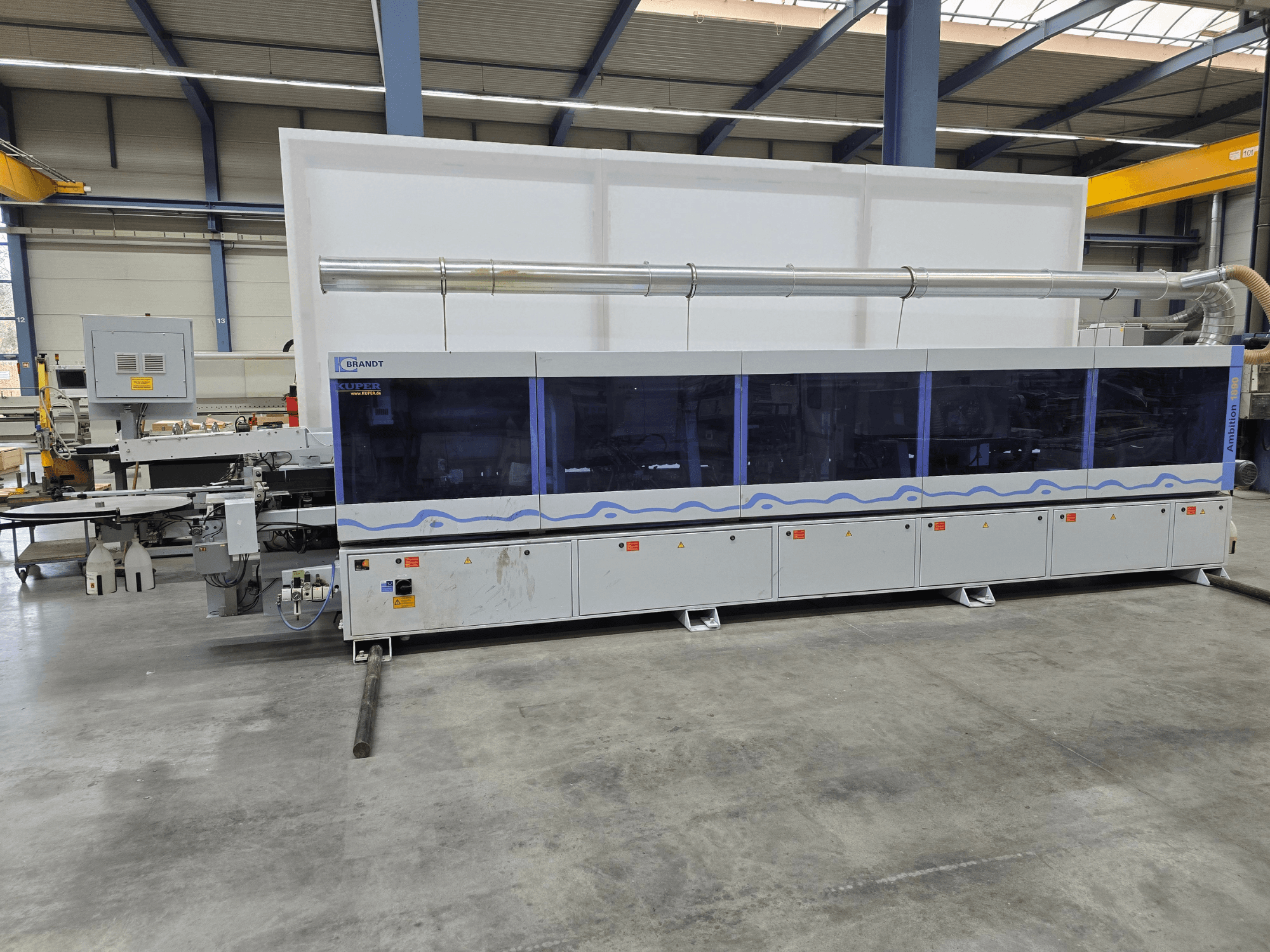 Brandt KUPER-Maschine in einer Fabrik, Frontansicht mit transparenten Paneelen, mit Bedientasten und Sicherheitshinweisen.
