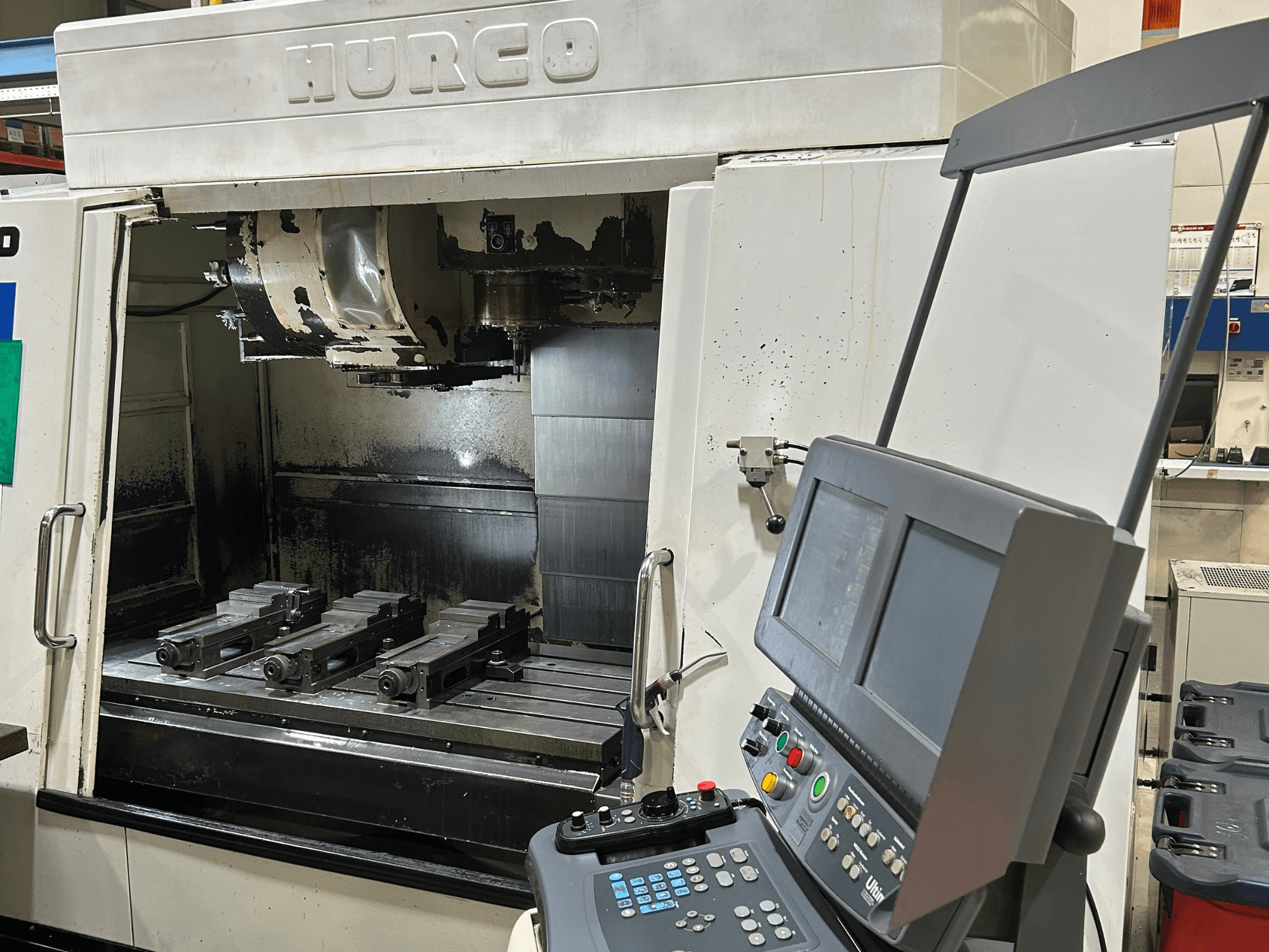Hurco CNC-Fräsmaschine, Vorderansicht, mit vier Werkzeughaltern auf dem Tisch und einem Bedienfeld mit zwei Bildschirmen und Tasten.
