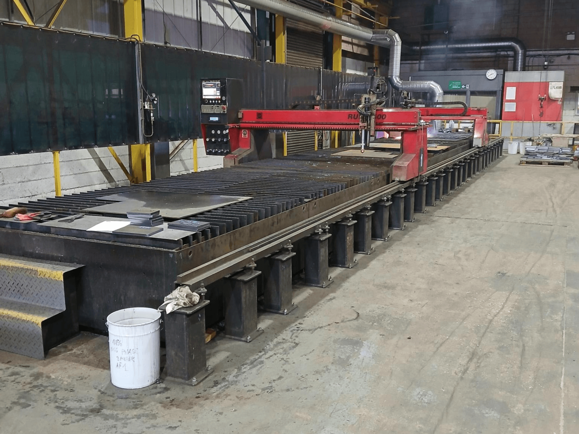 Rote RUIDA 300 Schneidemaschine, Seitenansicht, mit Blech auf einem Stahltisch, in einem industriellen Arbeitsbereich.