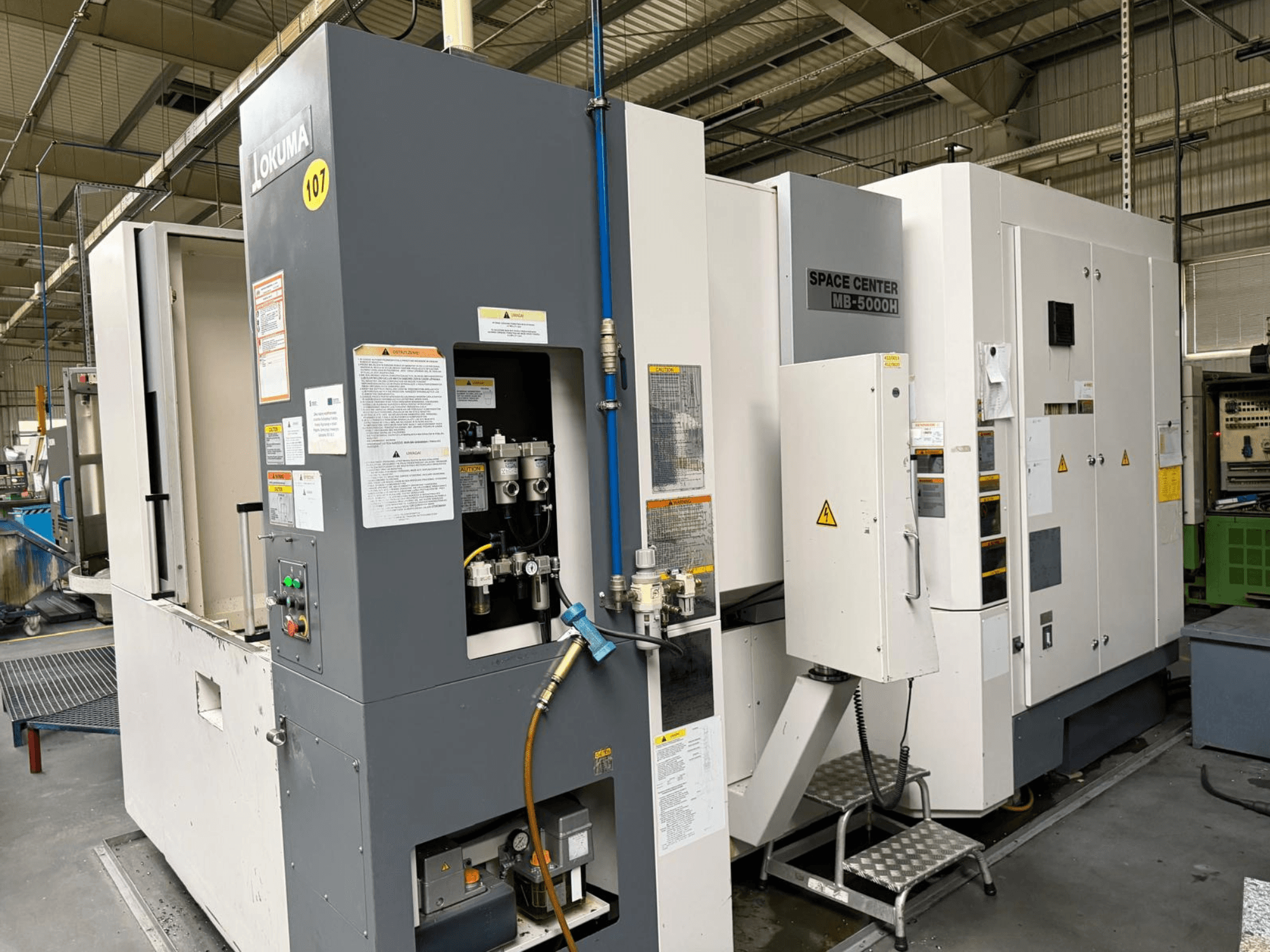 Horizontales Bearbeitungszentrum Okuma MB 5000H, Seitenansicht mit Bedienfeld und Maschinenkomponenten in einer Fabrikumgebung.