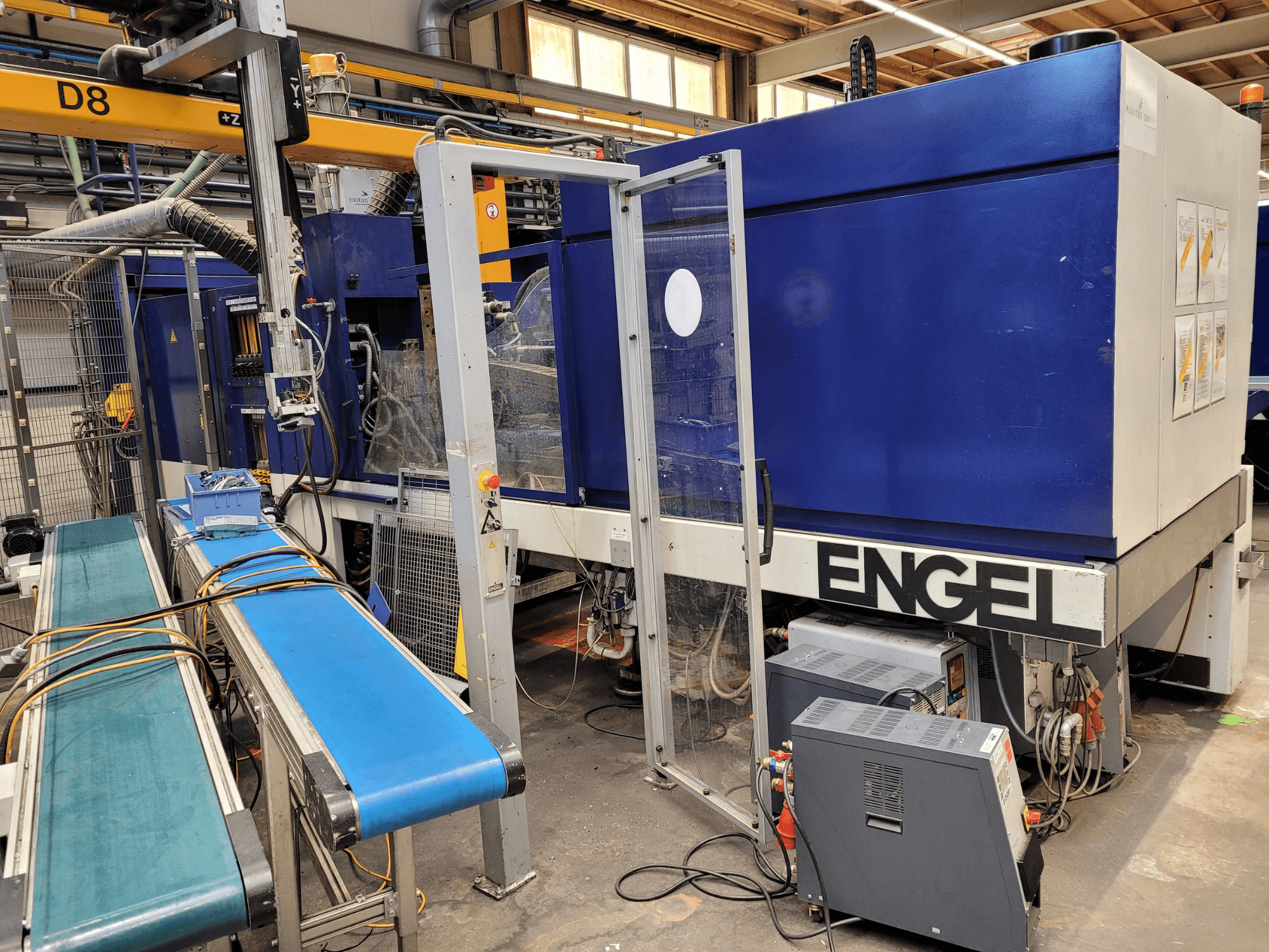 Blaue ENGEL-Maschine mit transparenter Schutztür, Seitenansicht, mit Bedienfeld, Förderband und sichtbaren elektrischen Anschlüssen.