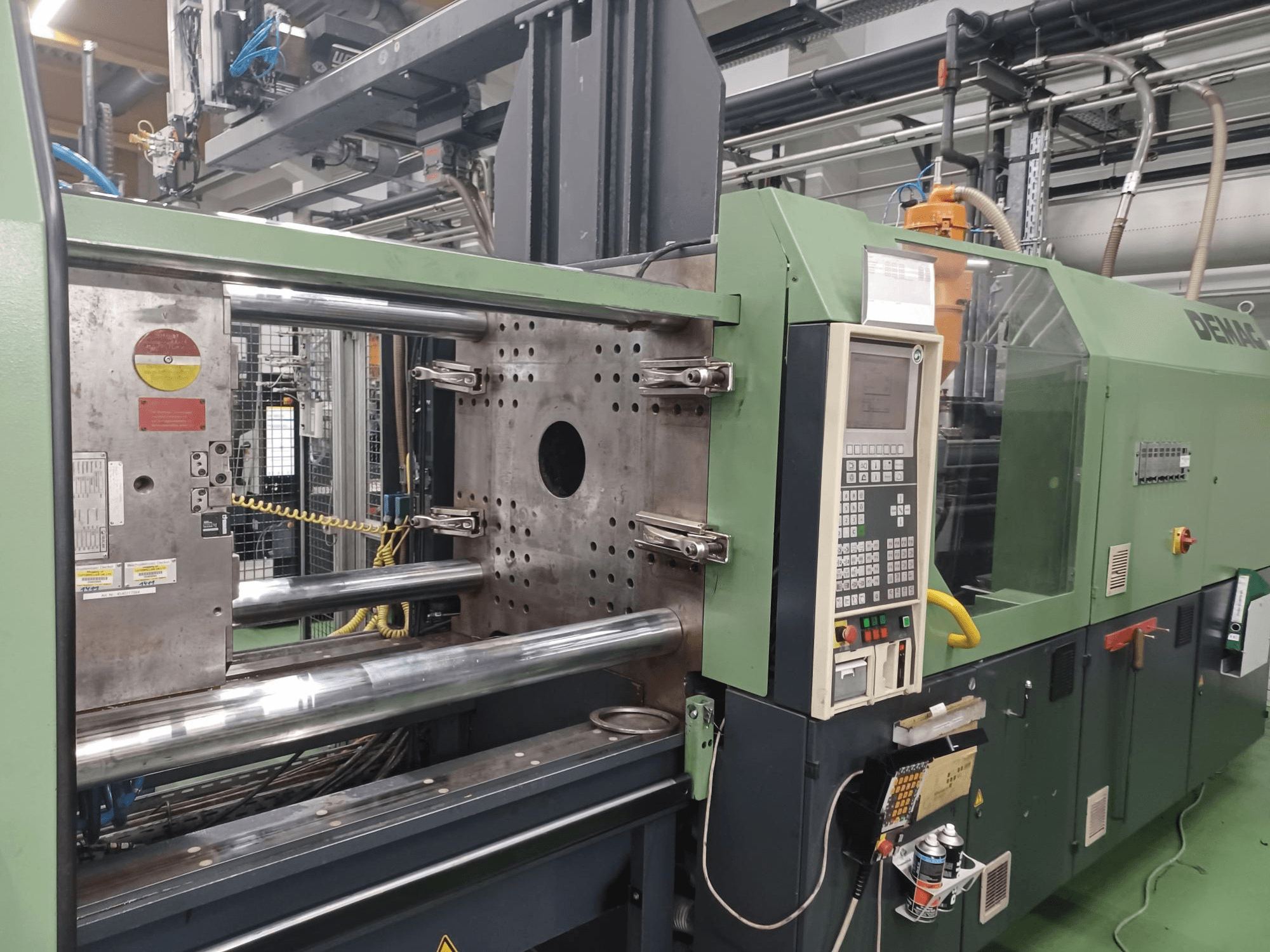 Demag-Spritzgießmaschine, Vorderansicht, mit Bedienpult, metallischen Hydraulikzylindern und Sicherheitseinrichtungen.