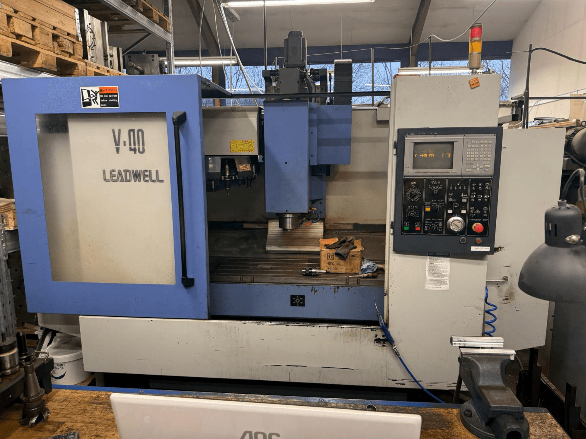 LEADWELL V-40 CNC-Fräsmaschine, Vorderansicht, mit einem Bedienfeld, Schneidwerkzeugen und einem Schraubstock auf einer Werkbank.