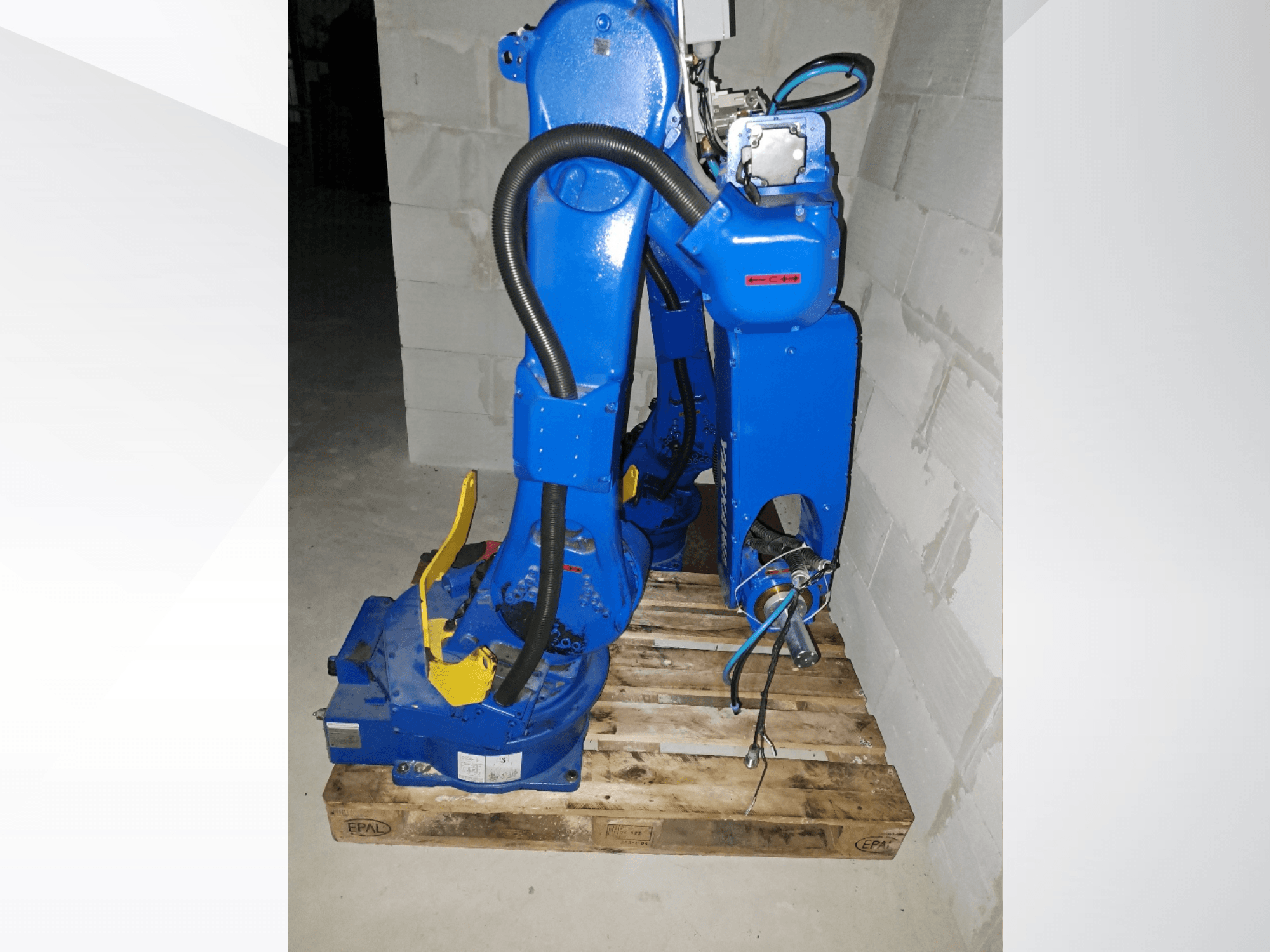 Yaskawa Motoman GP25-Roboterarm in Blau, Seitenansicht auf einer Holzpalette, mit Kabeln und mechanischen Gelenken.