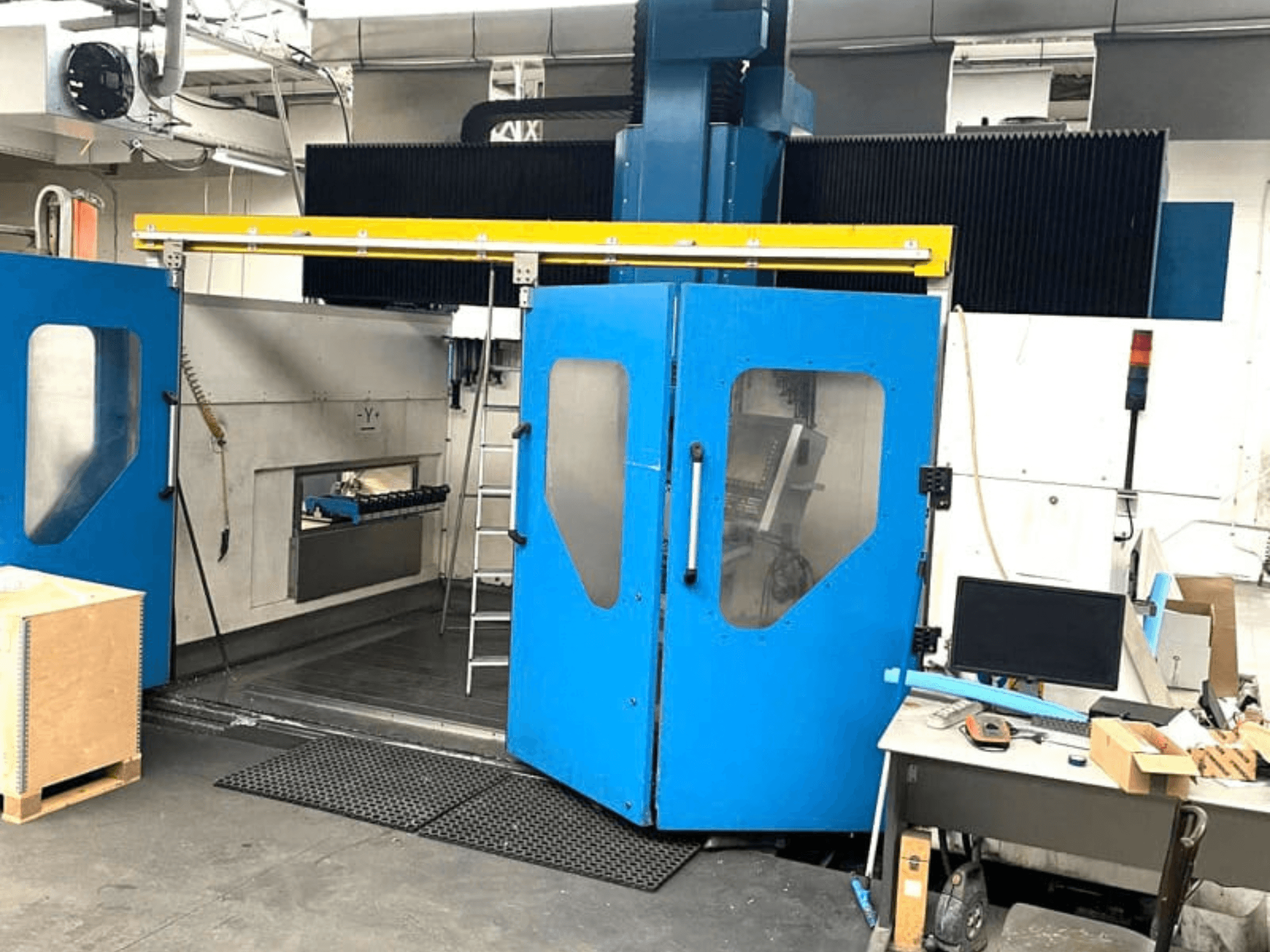 Vorderansicht des vertikalen Bearbeitungszentrums TECHMILL LABOR SHAPE 3220 mit geöffneten blauen Türen, die den Arbeitsbereich im Inneren freigeben.