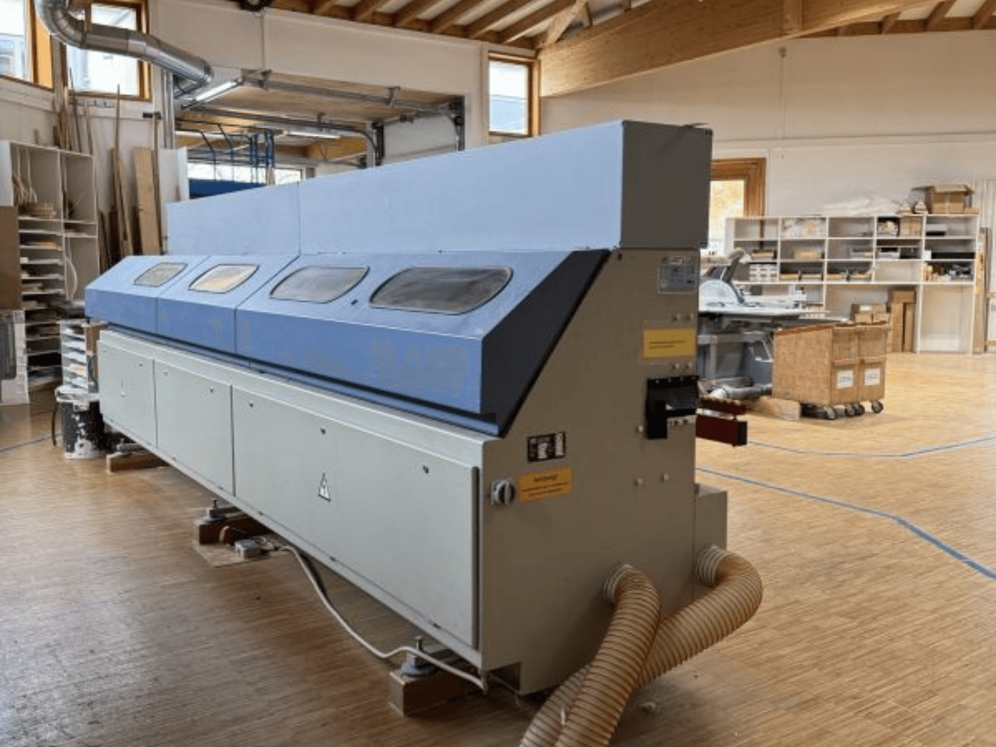 OTT Pacific V6-F Kantenanleimmaschine in der Seitenansicht; mit langem blauen Oberteil und Bedienfeld mit Schlauchanschluss.