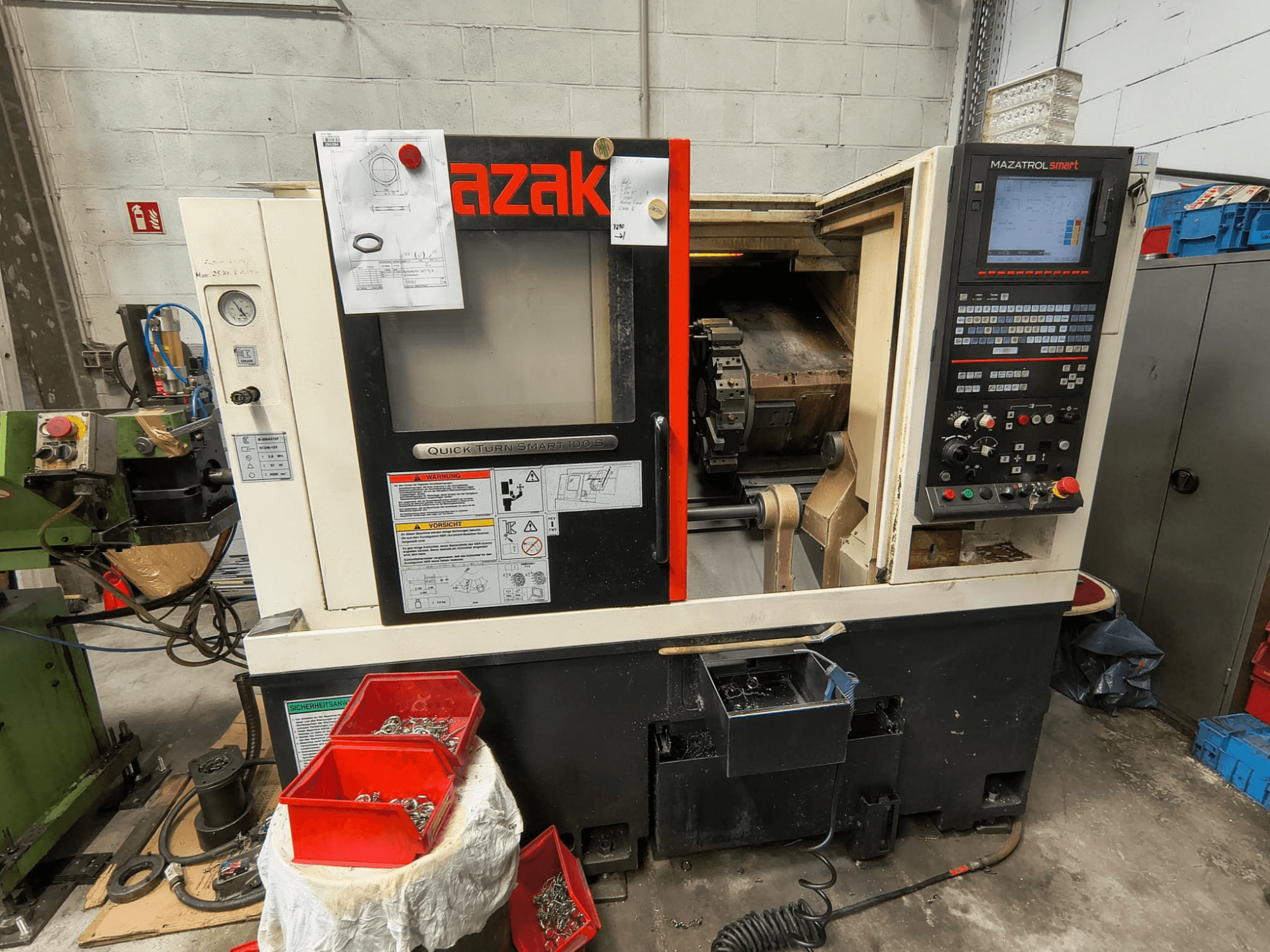 Mazak Quick Turn Smart 100 S, Seitenansicht mit Bedienfeld, Kühlmittelwanne und Aufbewahrungsbehältern für Schrauben.