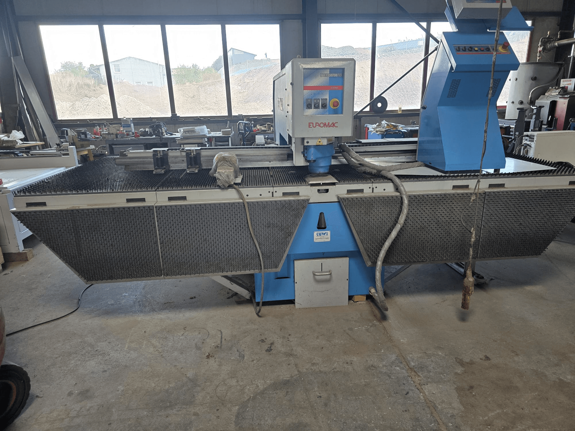 CNC-Stanzmaschine Euromac BX 1250/30 in einer Werkstatt, Seitenansicht mit Blick auf die Werkzeugsteuerung, das Industriedesign und das Metallschneidetisch.