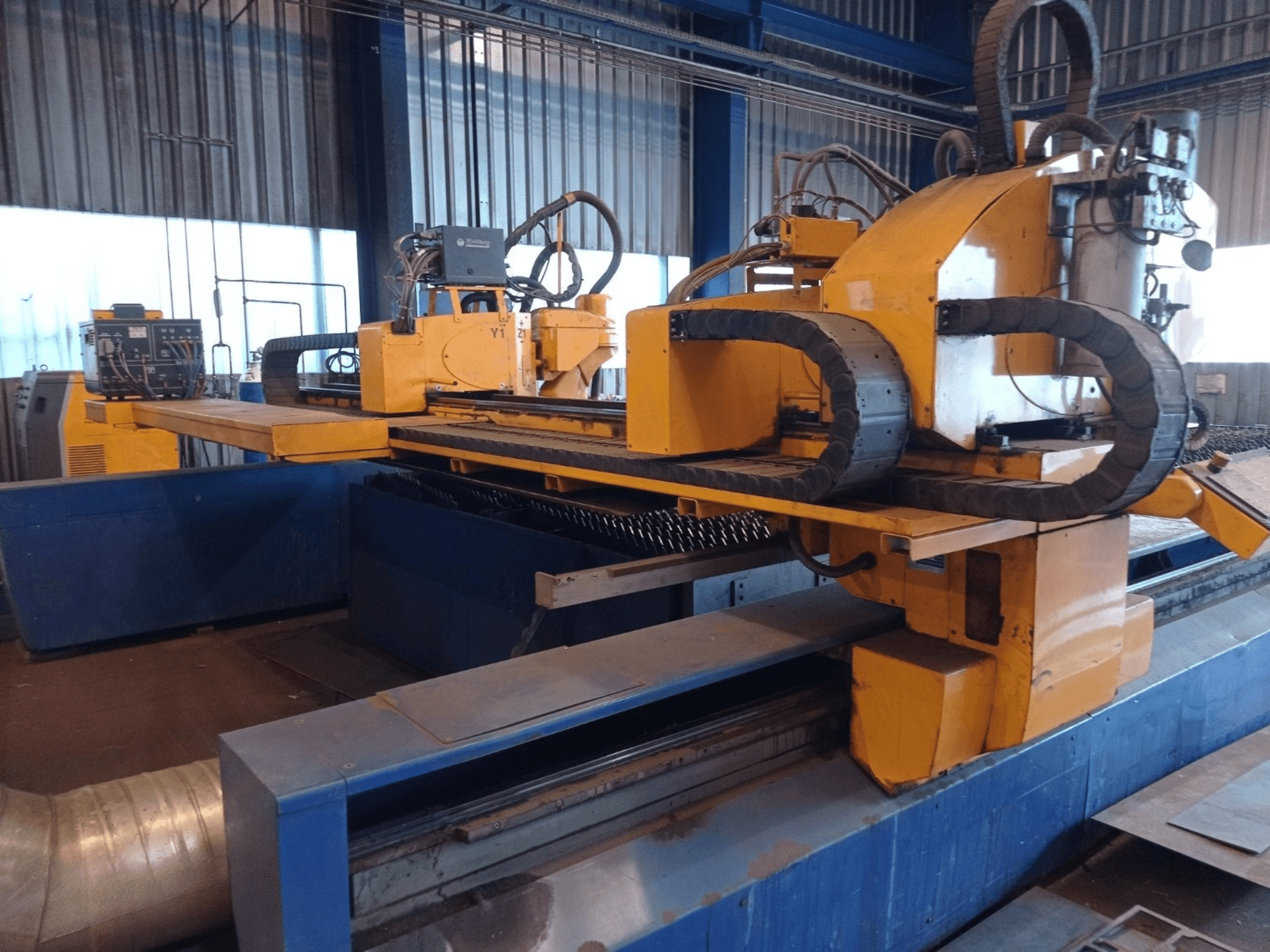 Gelbe CNC-Plasmaschneidmaschine mit zwei horizontalen Armen, von vorne gesehen, mit Bedienfeld und Schneidbett.