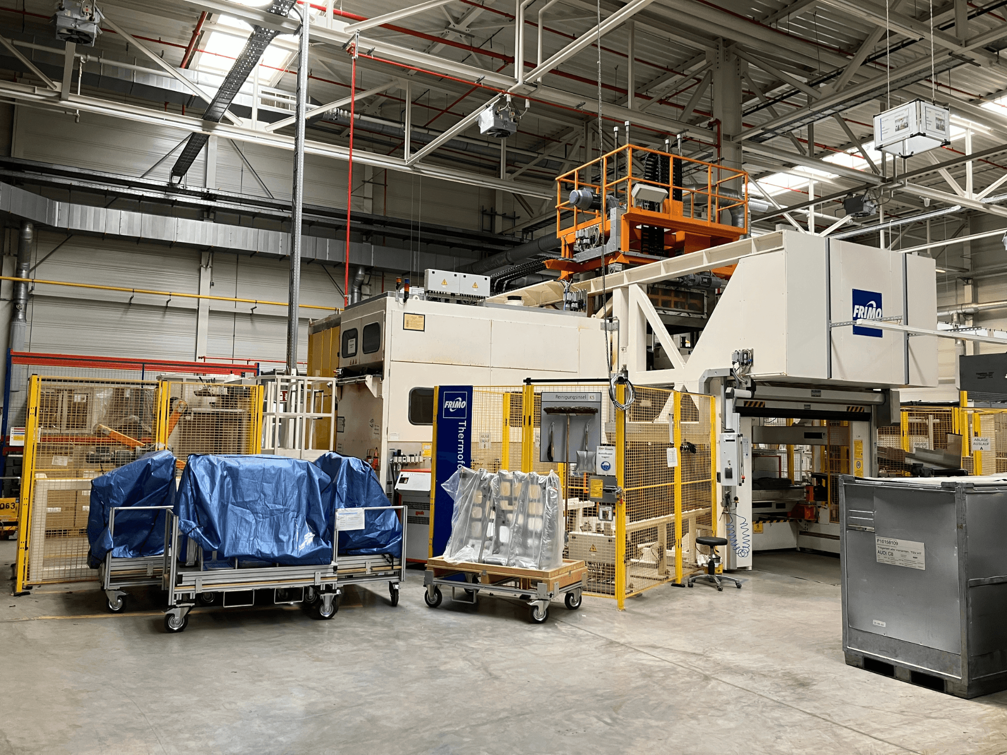 FRIMO FTL 80/200 Fullflex Kunststoffverarbeitungsanlage in einer Fabrik, Frontansicht mit blauen Planen und Sicherheitsbarrieren sichtbar.
