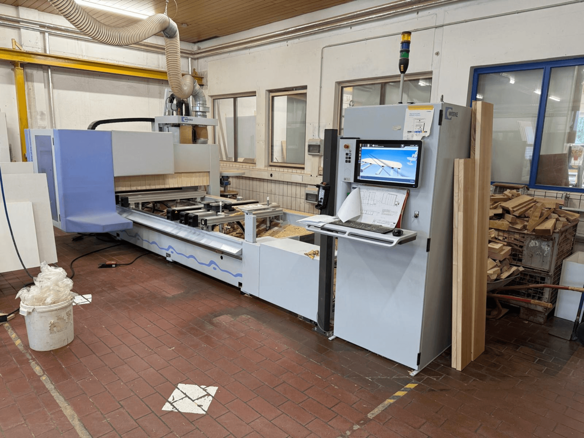 Weeke PROFI BMG211/32/12/K CNC-Holzbearbeitungszentrum, Vorderansicht, mit Bedienfeld und Holzstücken, ausgestattet mit einer Absauganlage.
