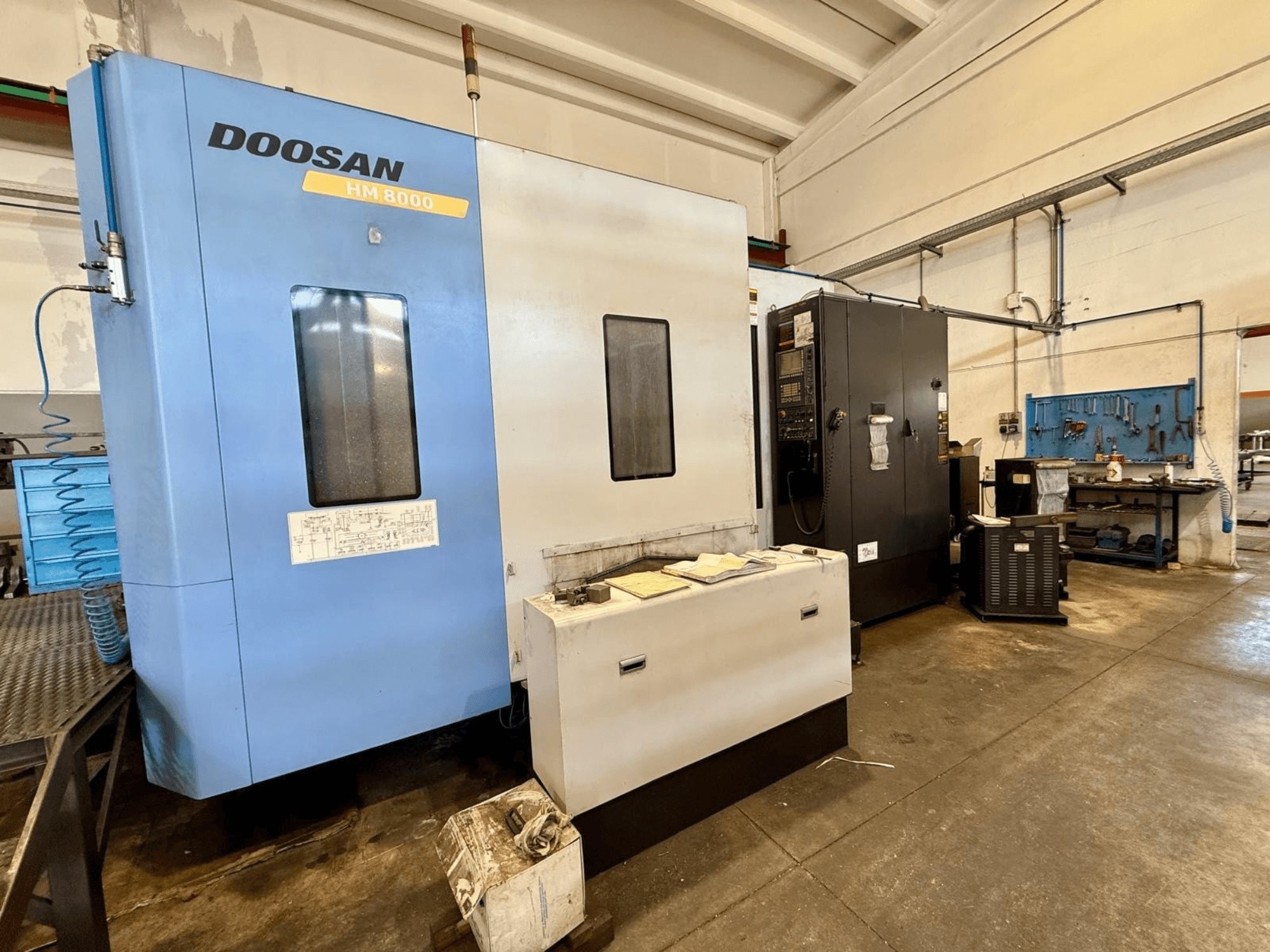 Horizontales Bearbeitungszentrum DOOSAN HM 8000 in Blau, Vorderansicht, mit Bedienfeld und angrenzenden Werkstattausrüstungen.