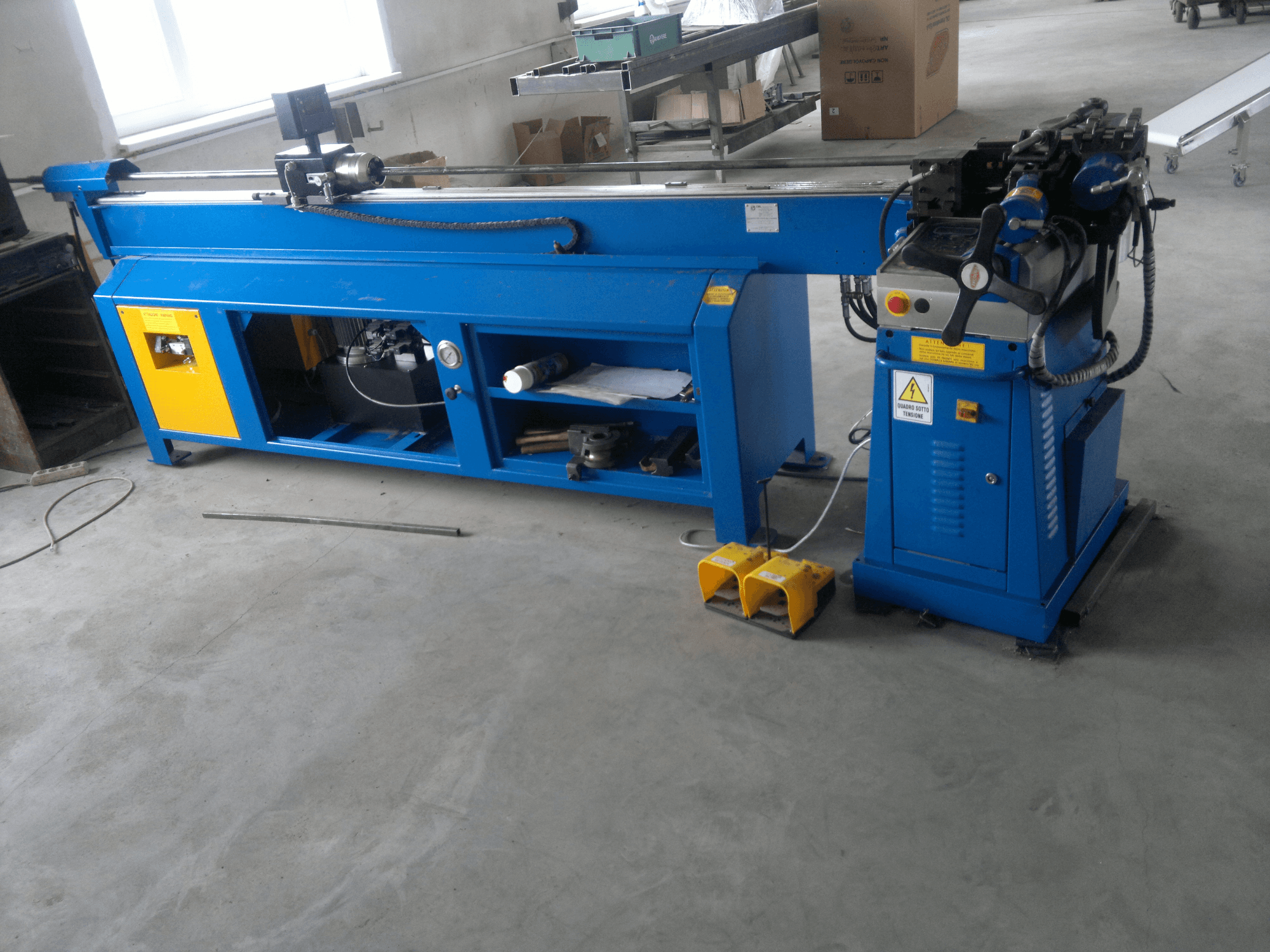 Blaue Holzbearbeitungsmaschine mit gelben Akzenten, Seitenansicht; mit Bedienfeld, Fußpedalen und einer rotierenden Messereinheit.