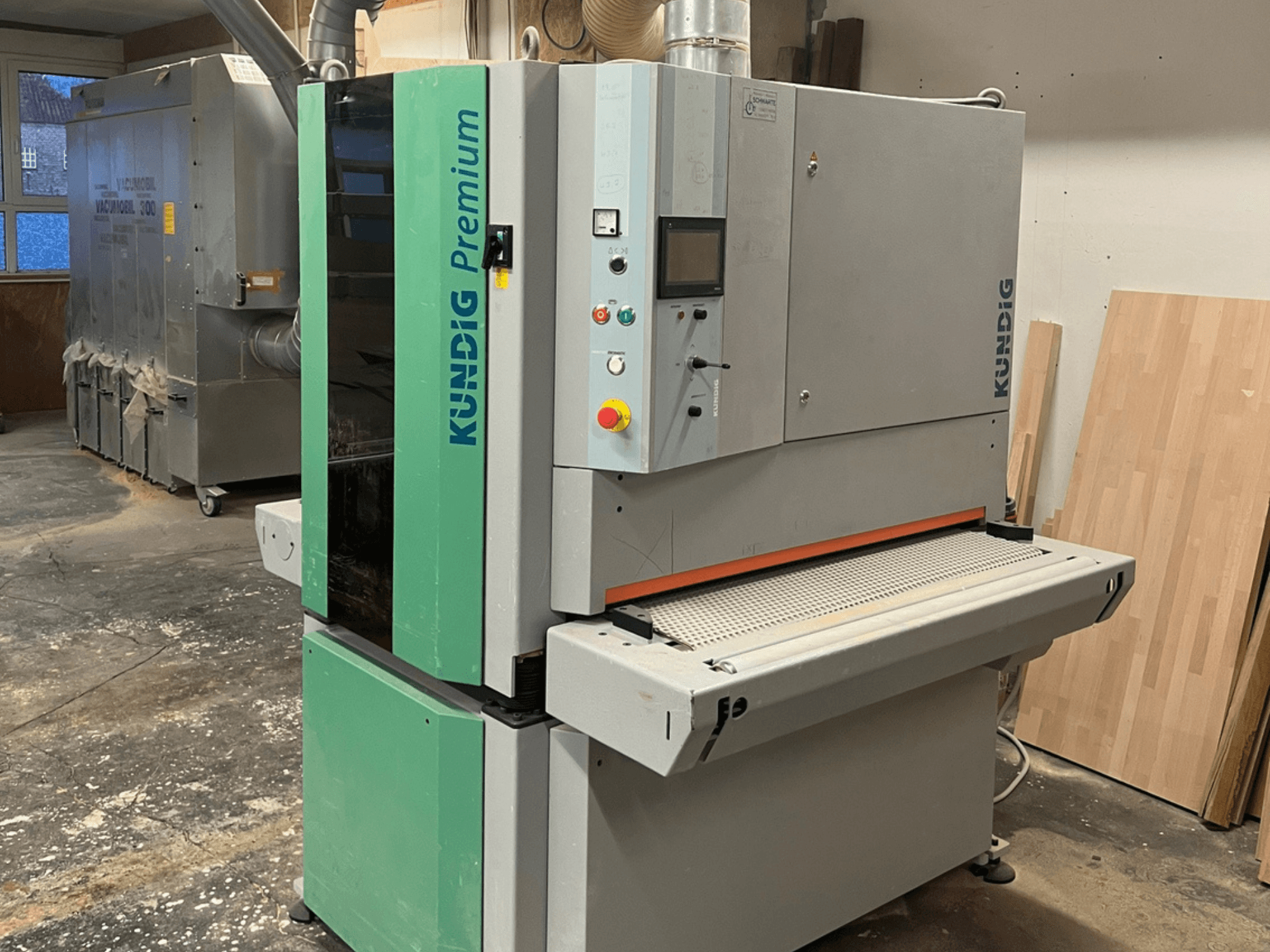 Kundig Premium-1 1100K Bandschleifmaschine in grau und grün, dargestellt in einer Seitenansicht mit Bedienfeld und Schleifband sichtbar.