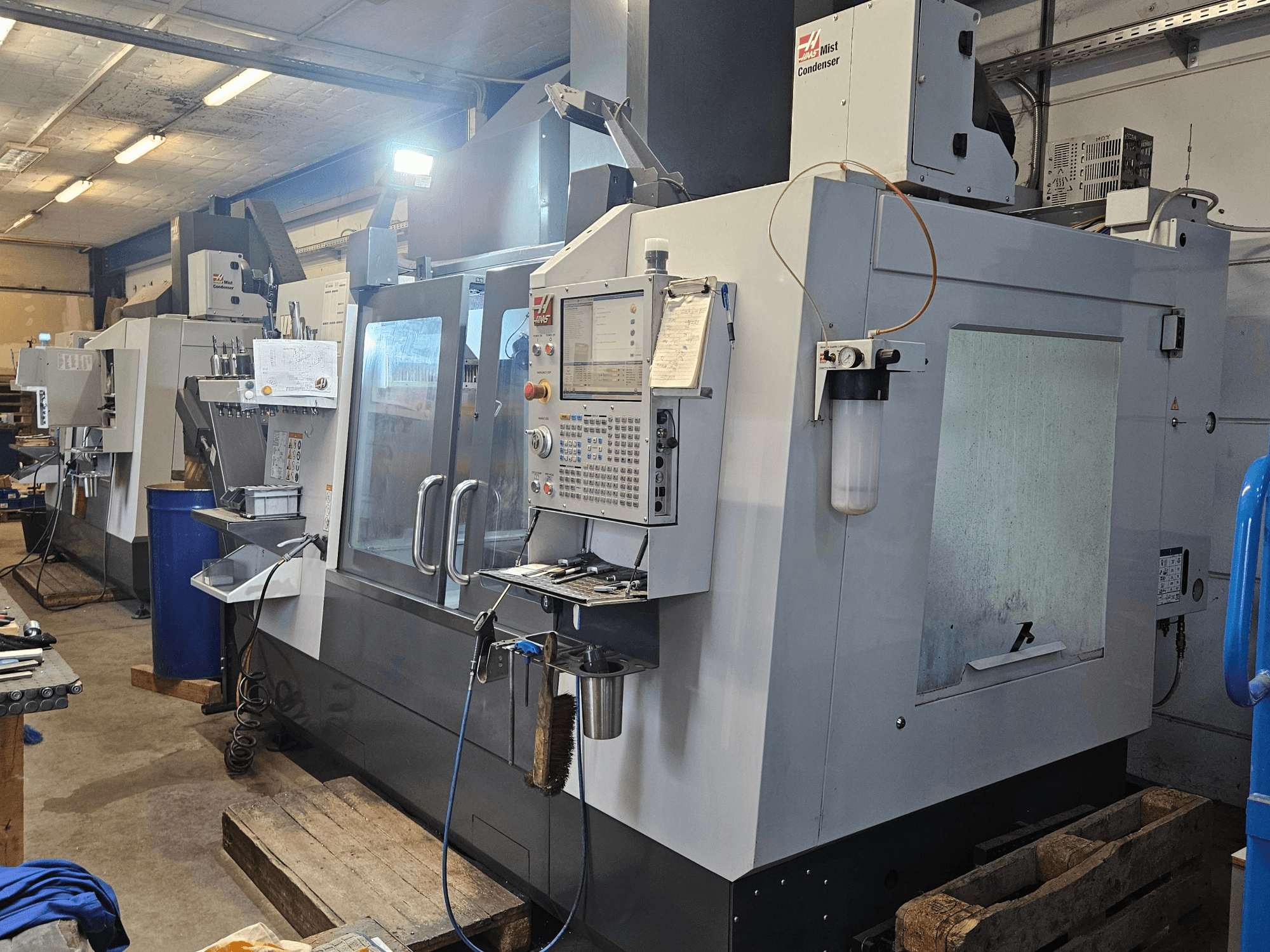 Vertikales Bearbeitungszentrum Haas VF-3YT/50 in einer Werkstatt, Vorderansicht mit Bedienfeld, Werkzeughaltern und Nebelkondensator.