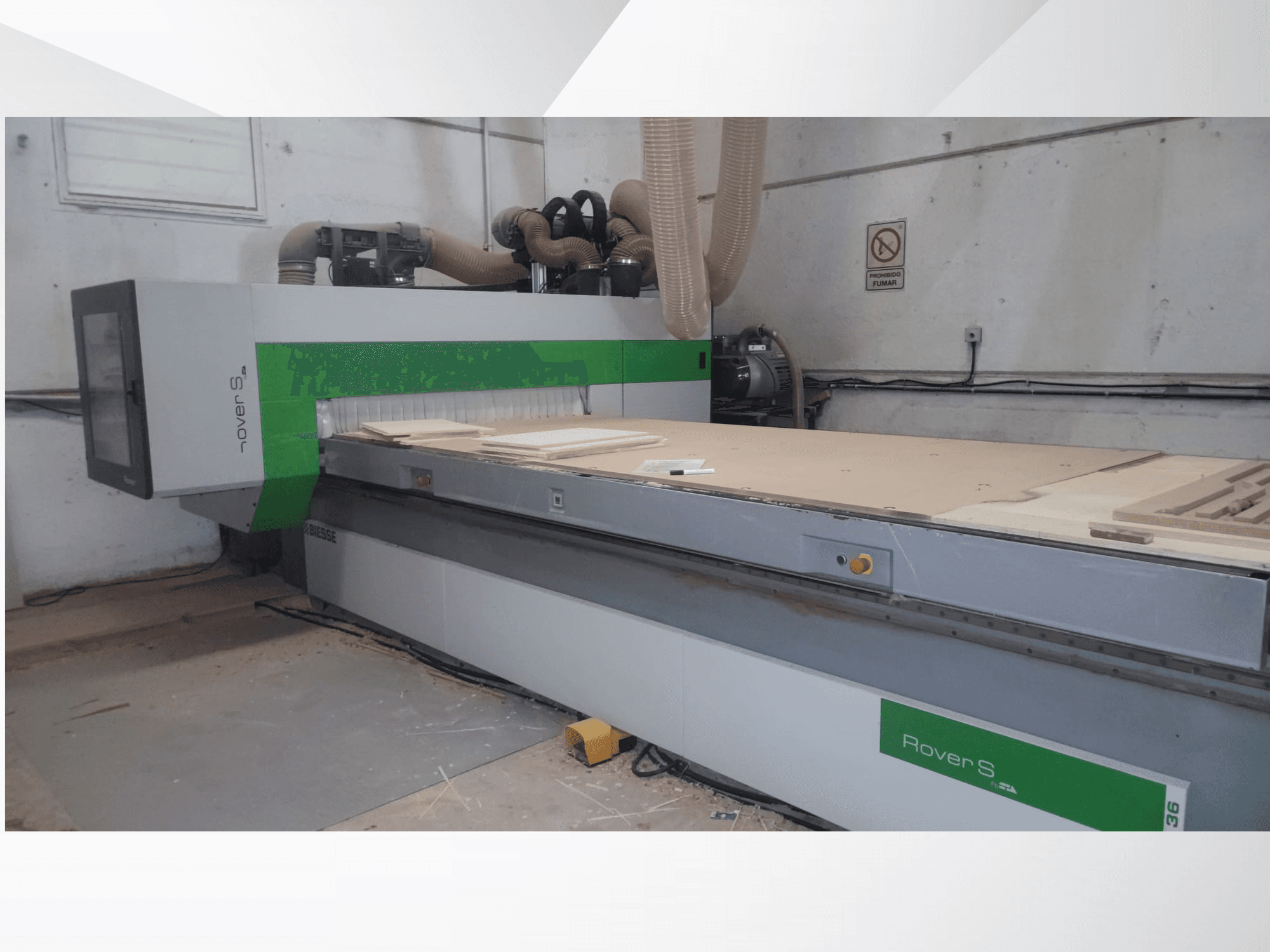 Vorderansicht der Biesse Rover S CNC-Maschine mit einer großen Arbeitsfläche mit Holzpaneelen und Absaugschläuchen.
