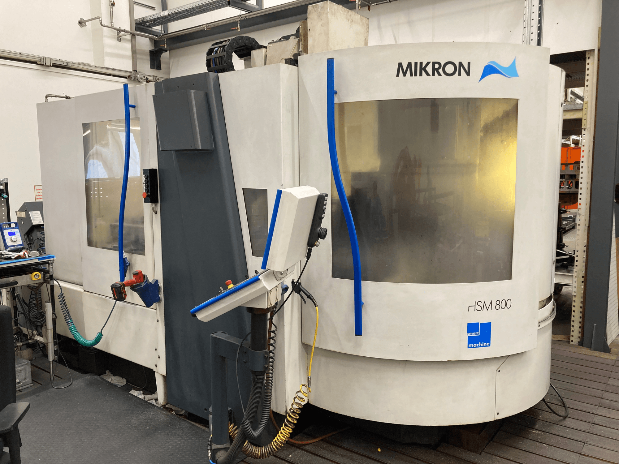 Mikron HSM 800, Seitenansicht eines CNC-Bearbeitungszentrums mit Bedienfeld und Werkzeughalter, sichtbare Schläuche und Kabel.