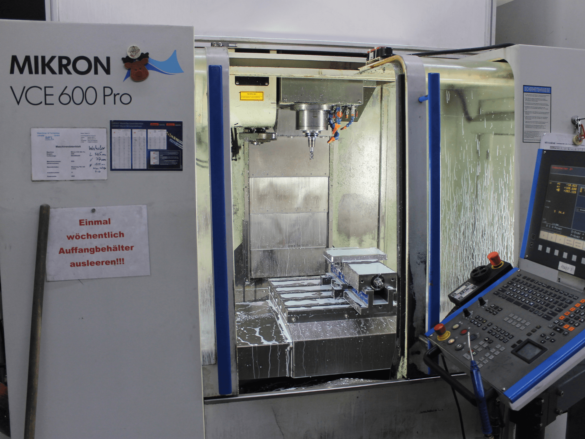 Mikron VCE 600 Pro Bearbeitungszentrum, Vorderansicht, mit Schneidwerkzeugen, Kühlmittelspray und Bedienfeld mit Tasten.
