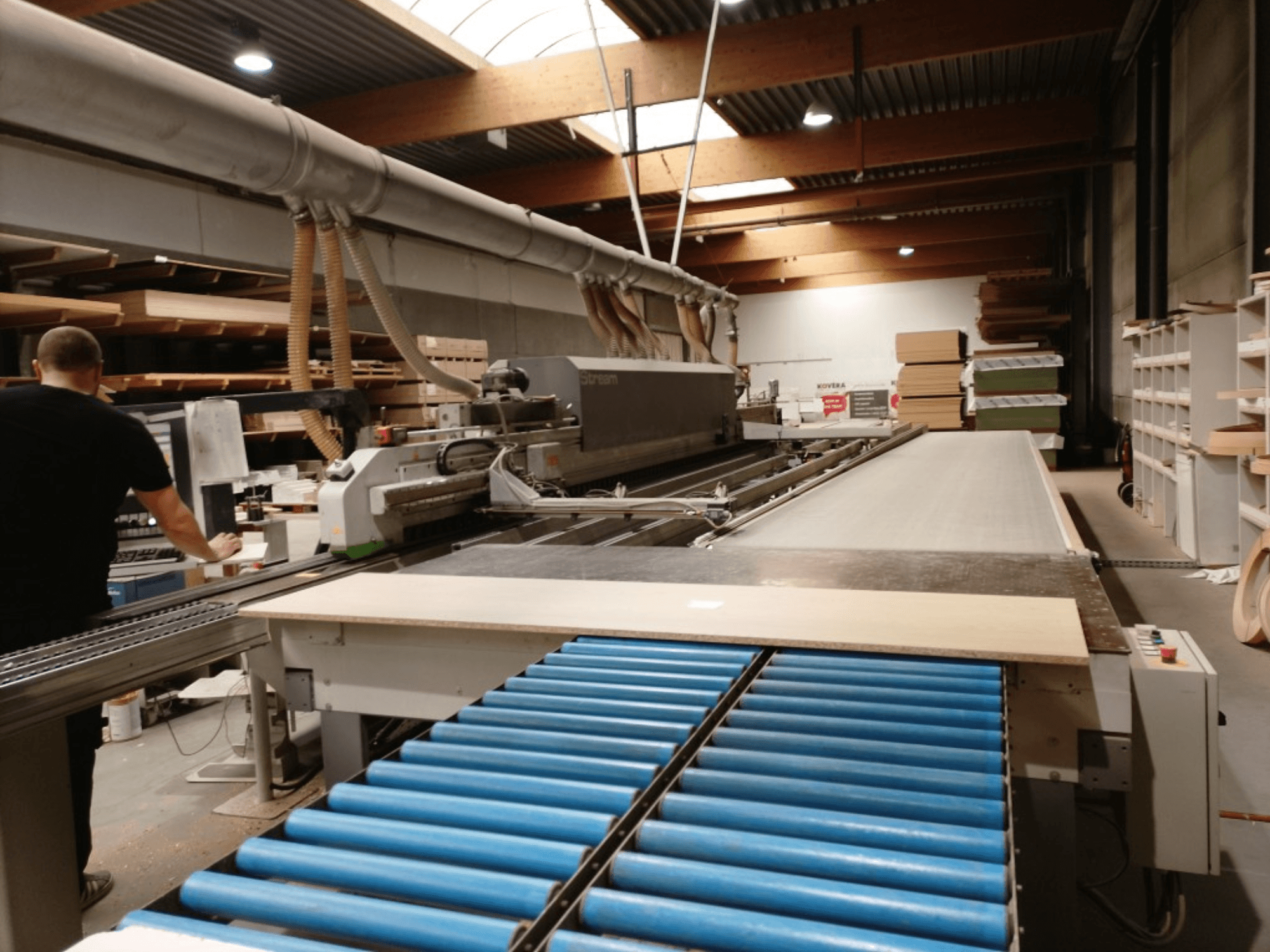 BIESSE Edge Stream B1 Kantenanleimmaschine, Seitenansicht mit Bediener, blauen Rollen und Holzplatte auf Förderband.