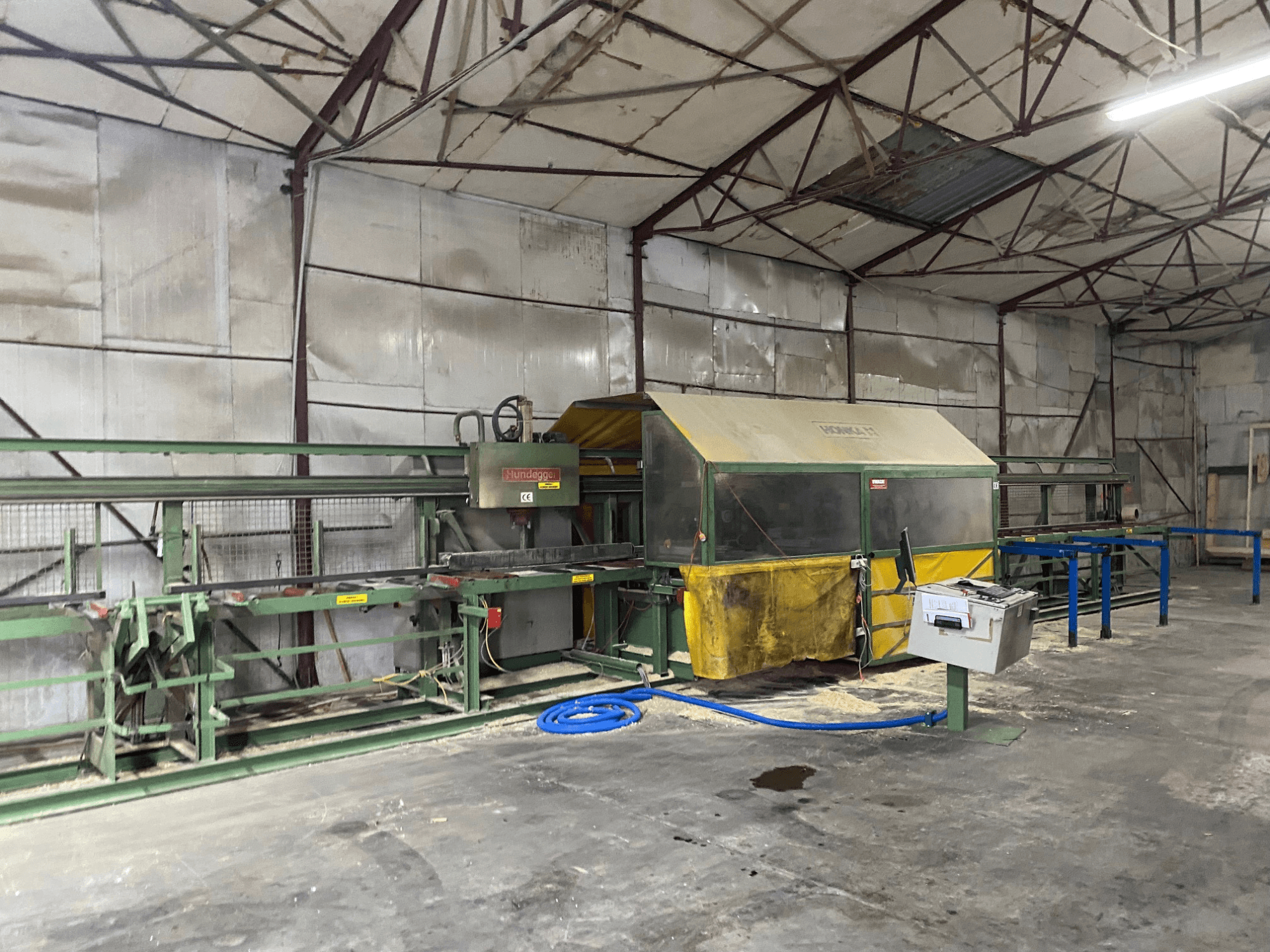 CNC-Holzbearbeitungszentrum HUNDEGGER K1 in einer Werkstatt, Seitenansicht mit Maschinen, Bedienelementen und Sägemehl auf dem Boden.