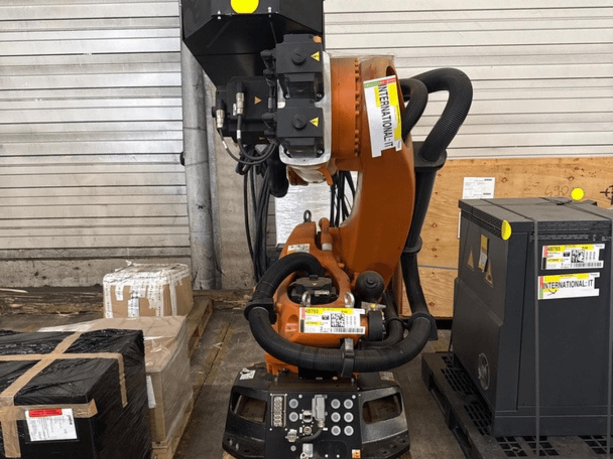 KUKA KR 210 R2700 – zusätzlicher Roboterarm in der Vorderansicht, ausgestellt auf einer Palette neben Verpackungen und Ausrüstung.