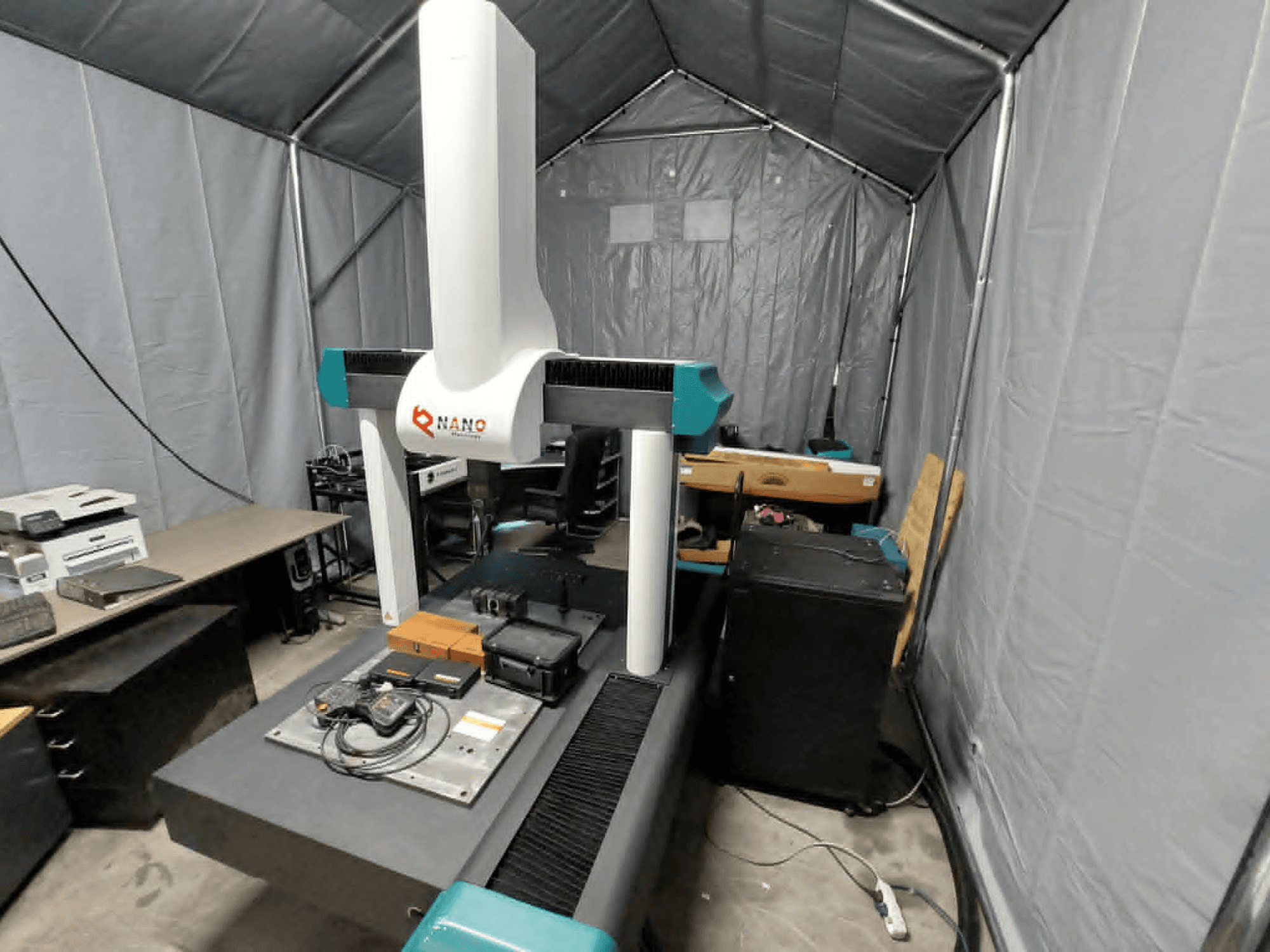 NANO METROLOGY Micr 7106 CMM in einem Zelt; Vorderansicht, die den Arm und die Messplattform der Maschine mit Zubehör zeigt.