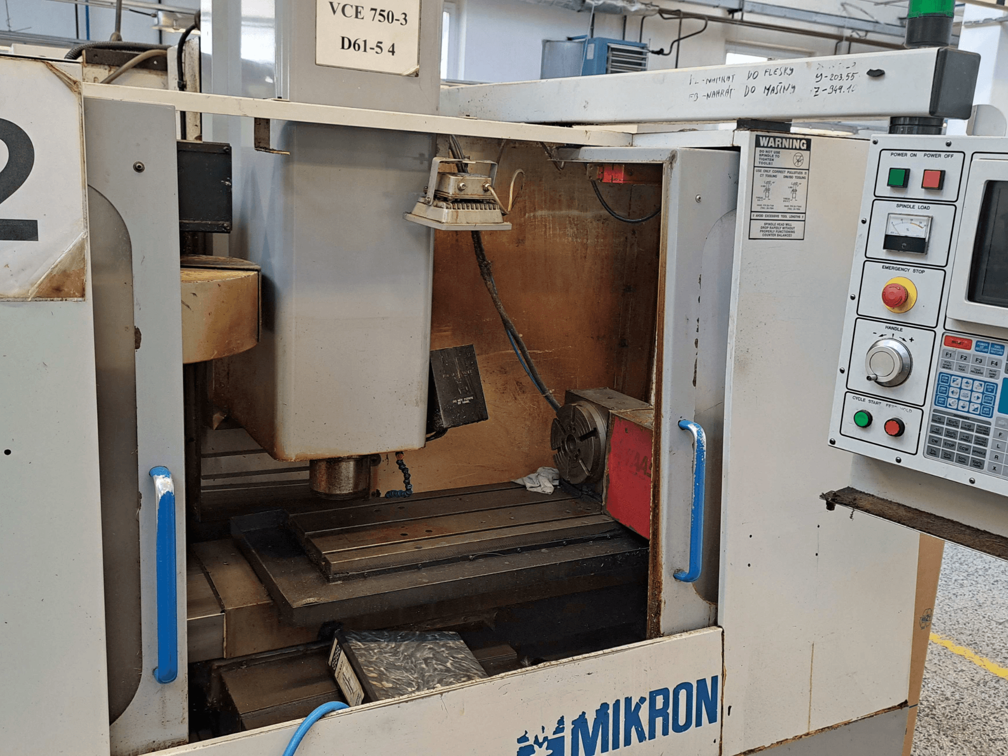 Frontansicht einer Mikron VCE 750-3 Fräsmaschine mit Spindel, Bedienfeld und Arbeitstisch mit technischen Details.