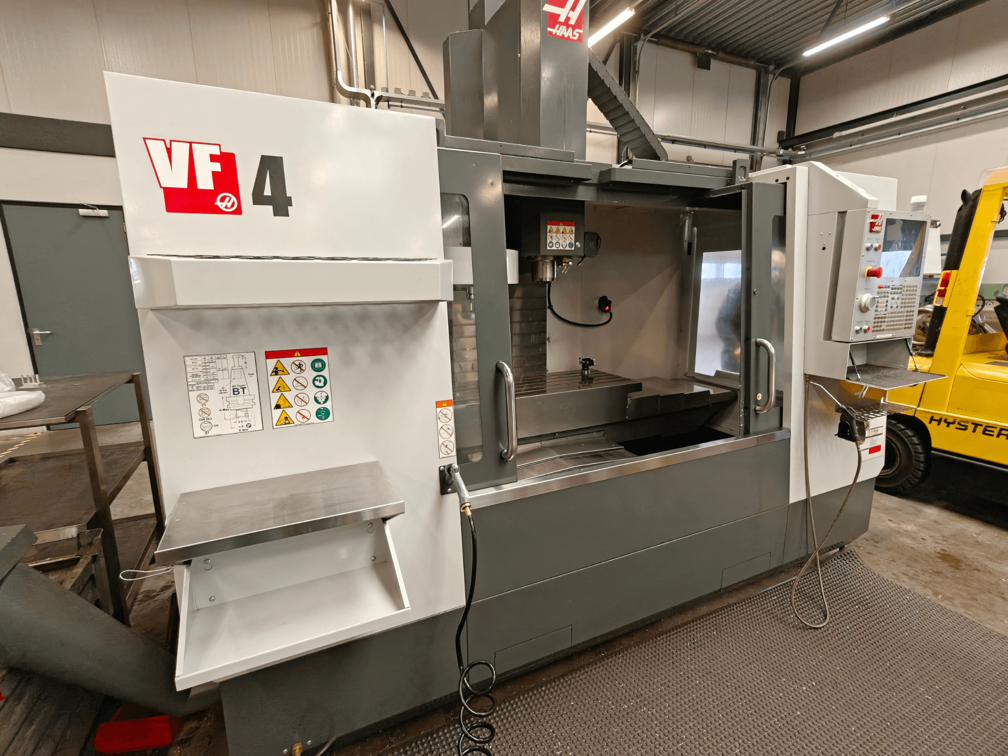 HAAS VF-4 Vertikal-Bearbeitungszentrum, Vorderansicht, mit Bedienfeld, Arbeitsbereich und Sicherheitsaufkleber an der Seite.