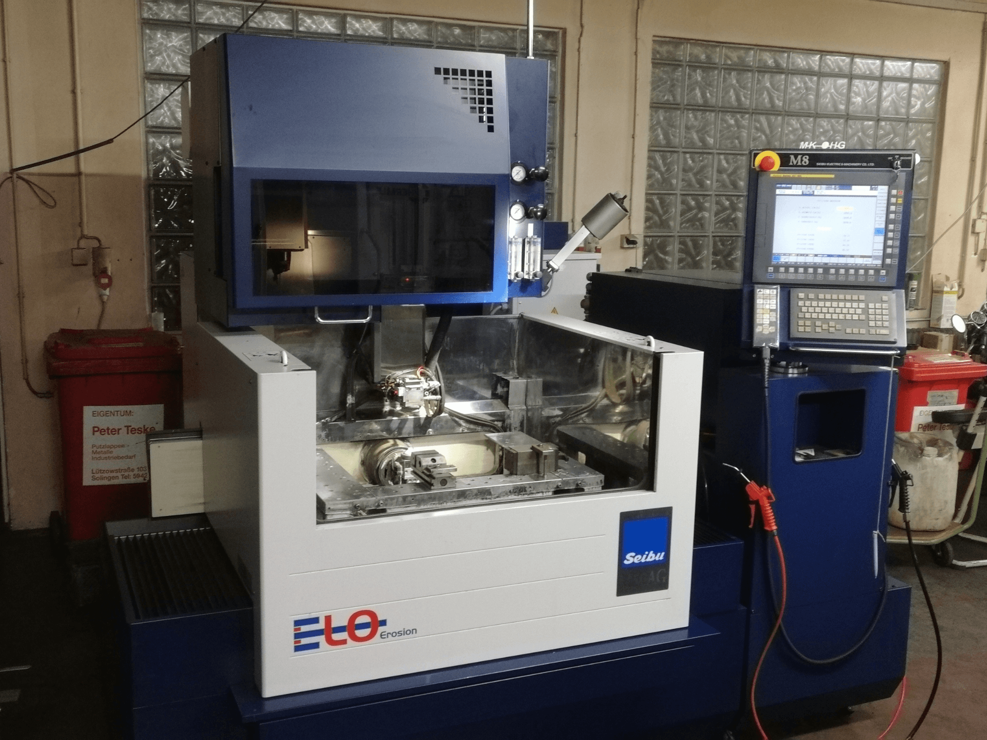 ELO Seibu Erodiermaschine von vorne gesehen, mit Bedienfeld und sichtbarem Arbeitsbereich mit Metallteilen.